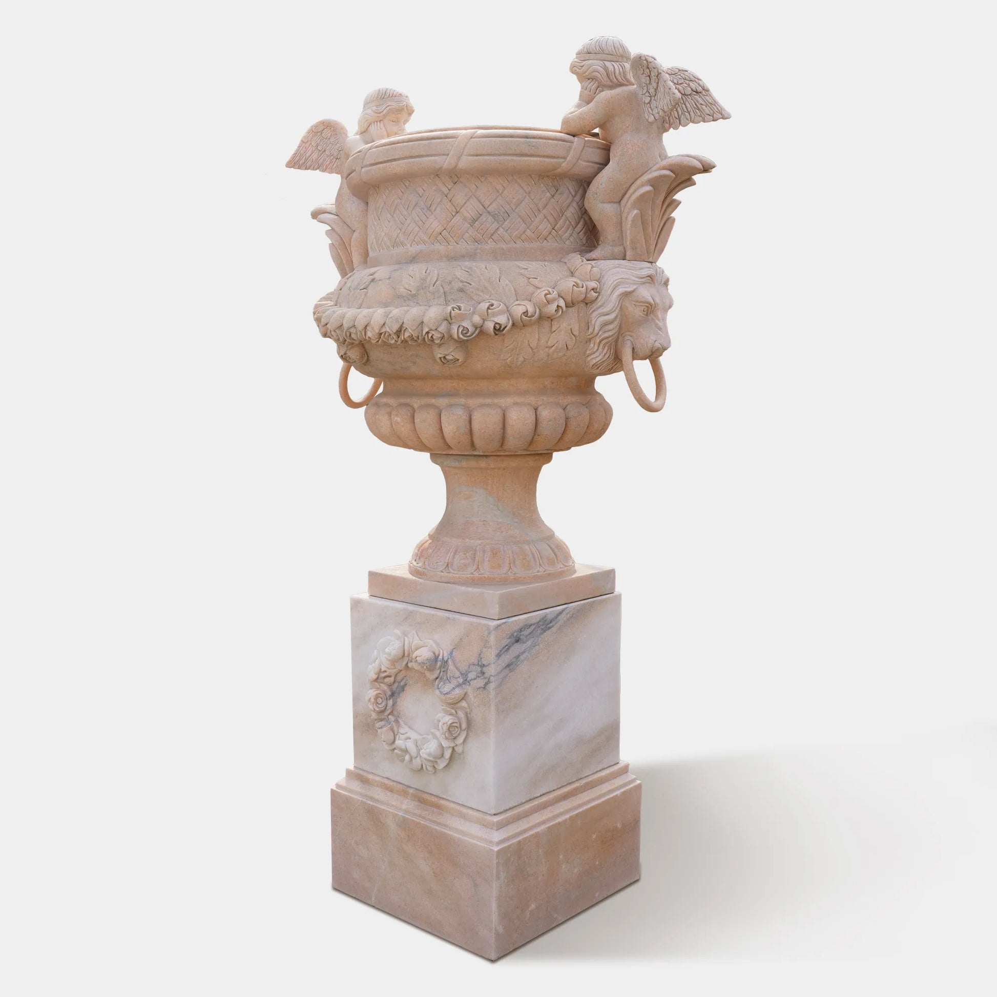 Marble planter sculpture with angel figures, lion head carvings, and floral relief base, displayed at a villa entrance with plants inside.