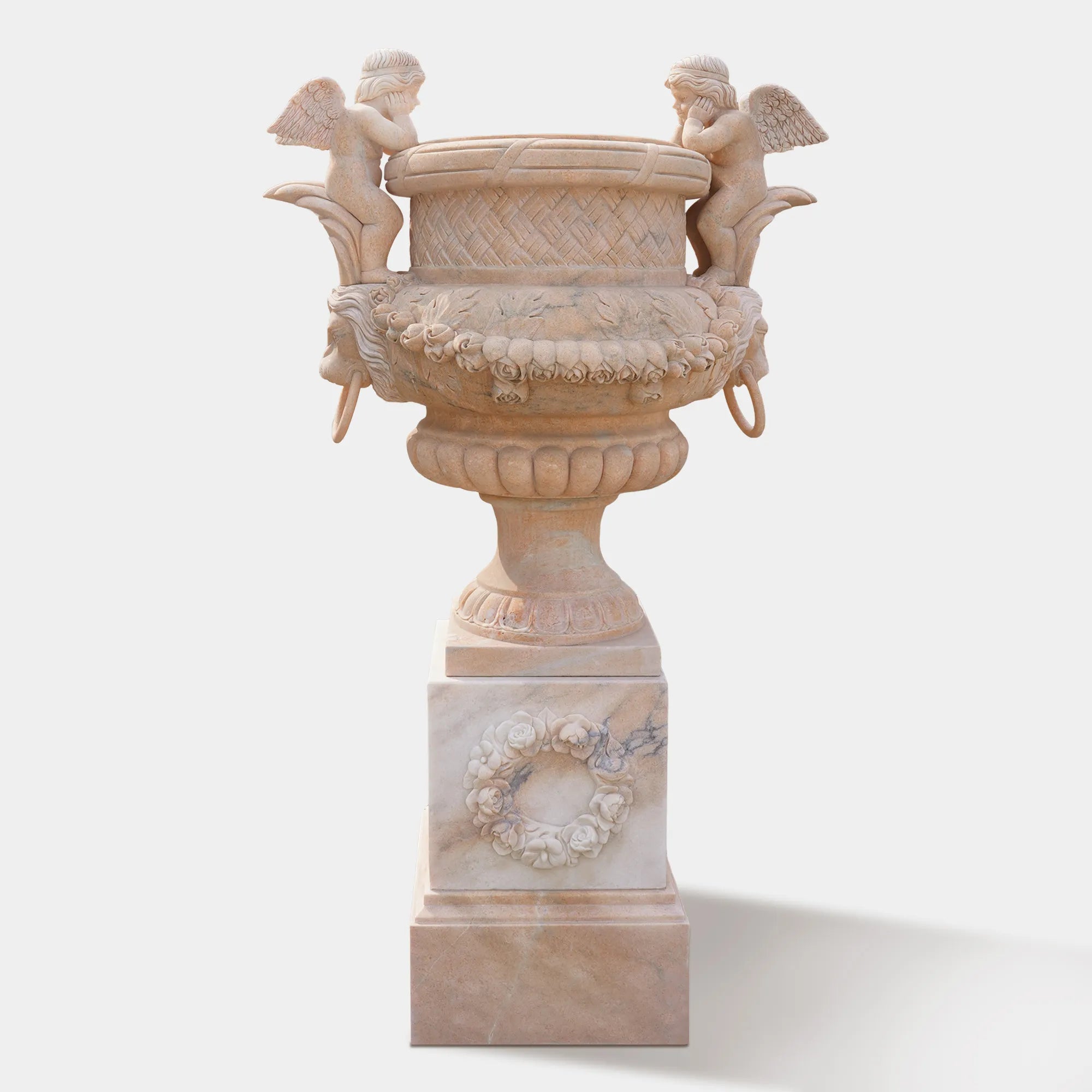 Marble planter sculpture with angel figures, lion head carvings, and floral relief base, displayed at a villa entrance with plants inside.