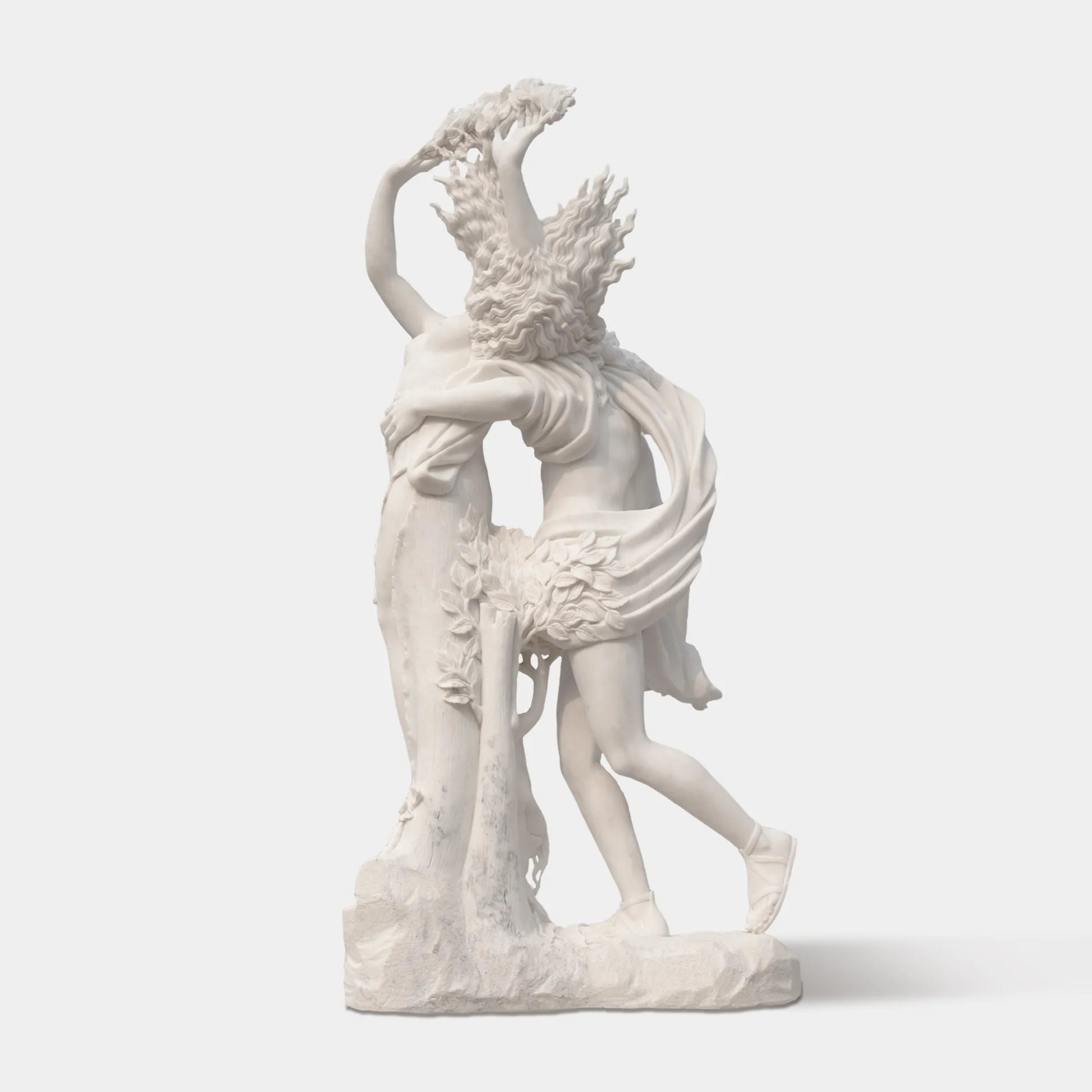 Marble sculpture of Apollo and Daphne in transformation, showing Apollo reaching for Daphne as she turns into a laurel tree, displayed outdoors in a classical courtyard with marble arches and palm trees.