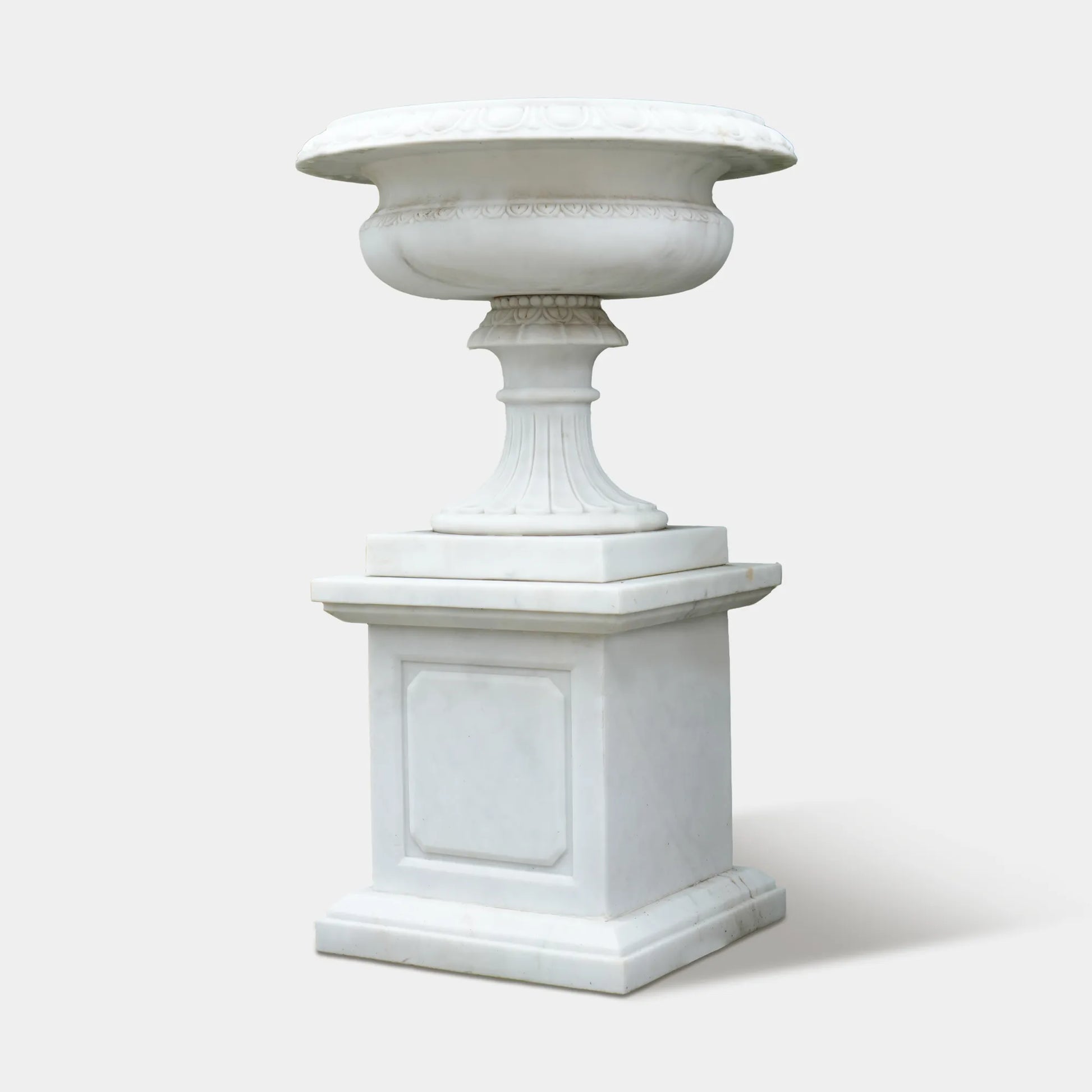 Marble planter sculpture filled with blue hydrangeas beside a stone villa entrance.