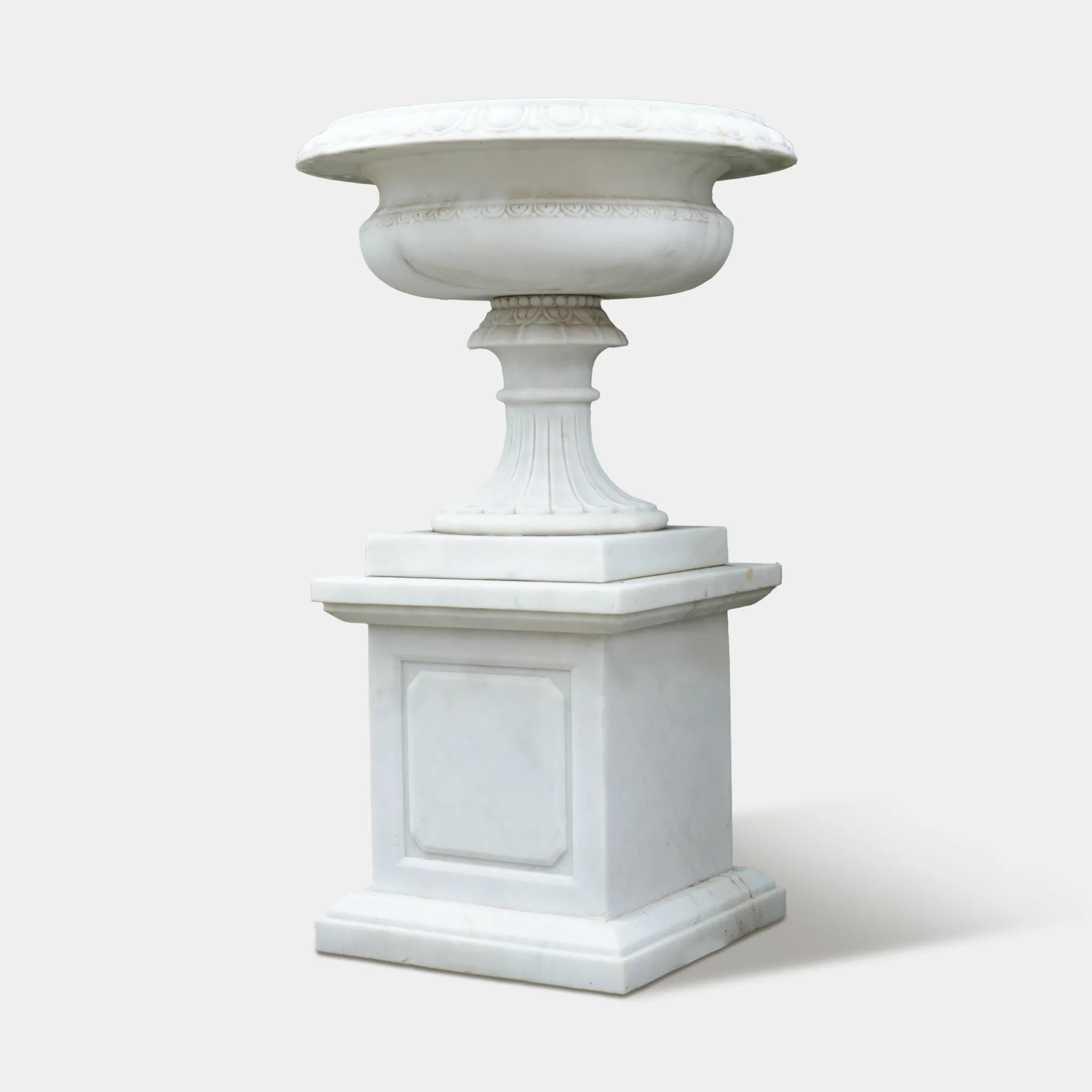 Marble planter sculpture filled with blue hydrangeas beside a stone villa entrance.