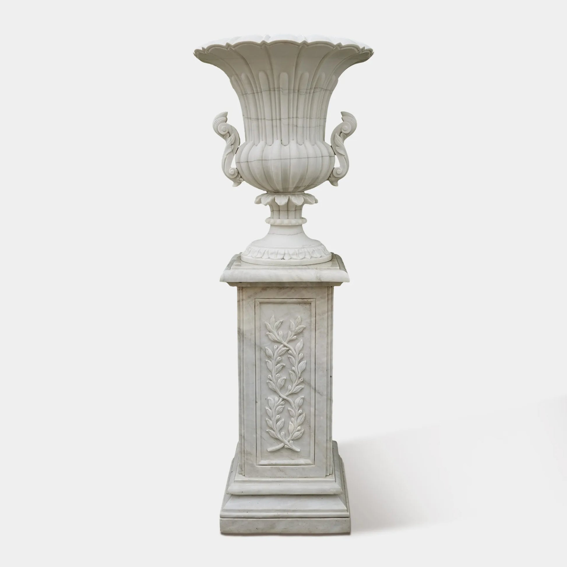 Pair of marble planter sculptures with white flowers framing a garden pathway.