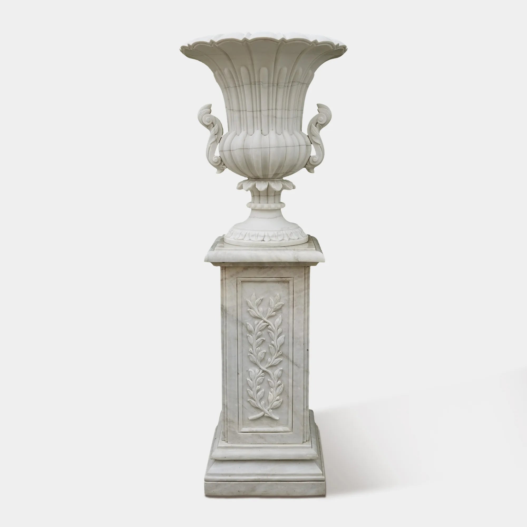 Pair of marble planter sculptures with white flowers framing a garden pathway.