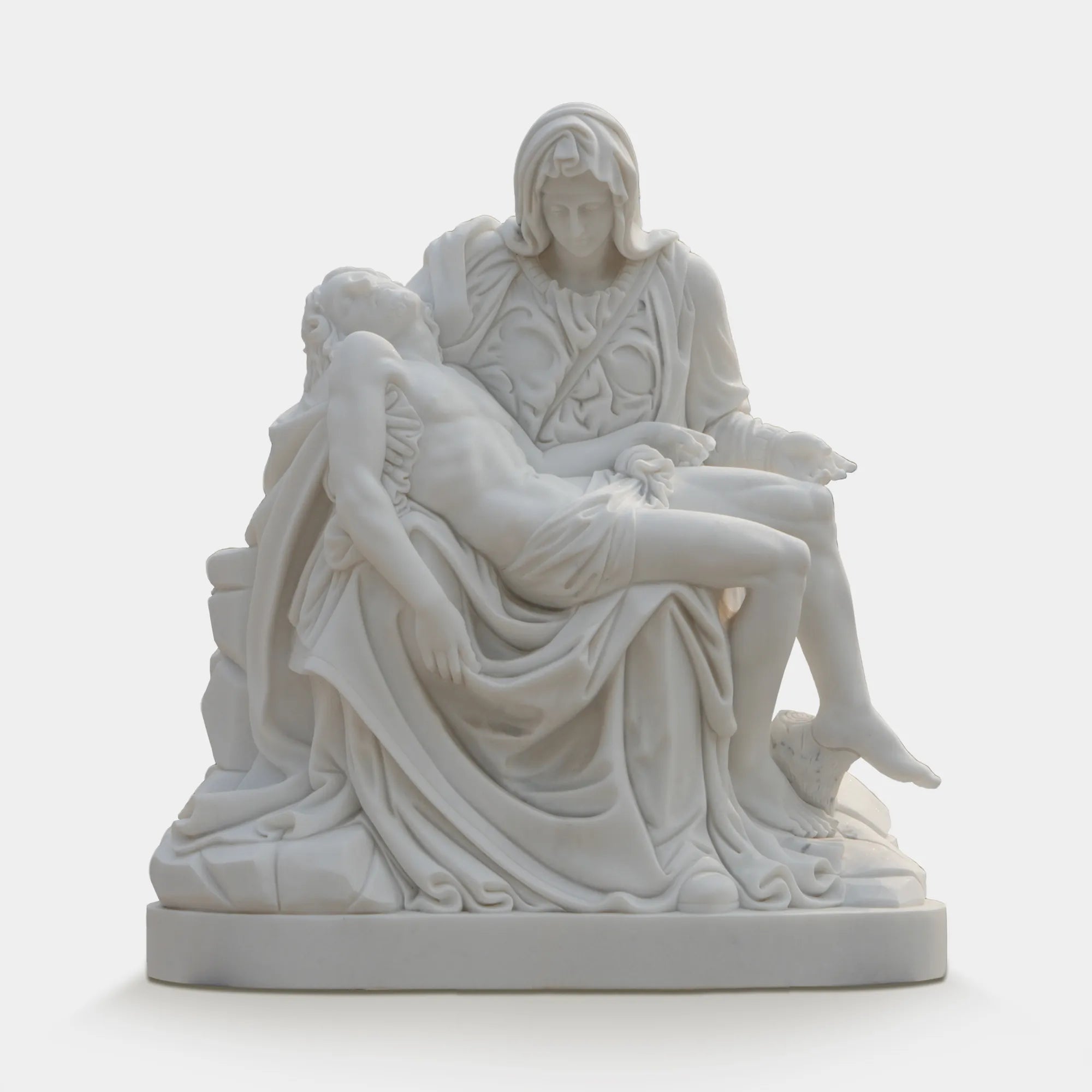 Marble Pietà sculpture placed in a tranquil garden with sunlight filtering through trees.