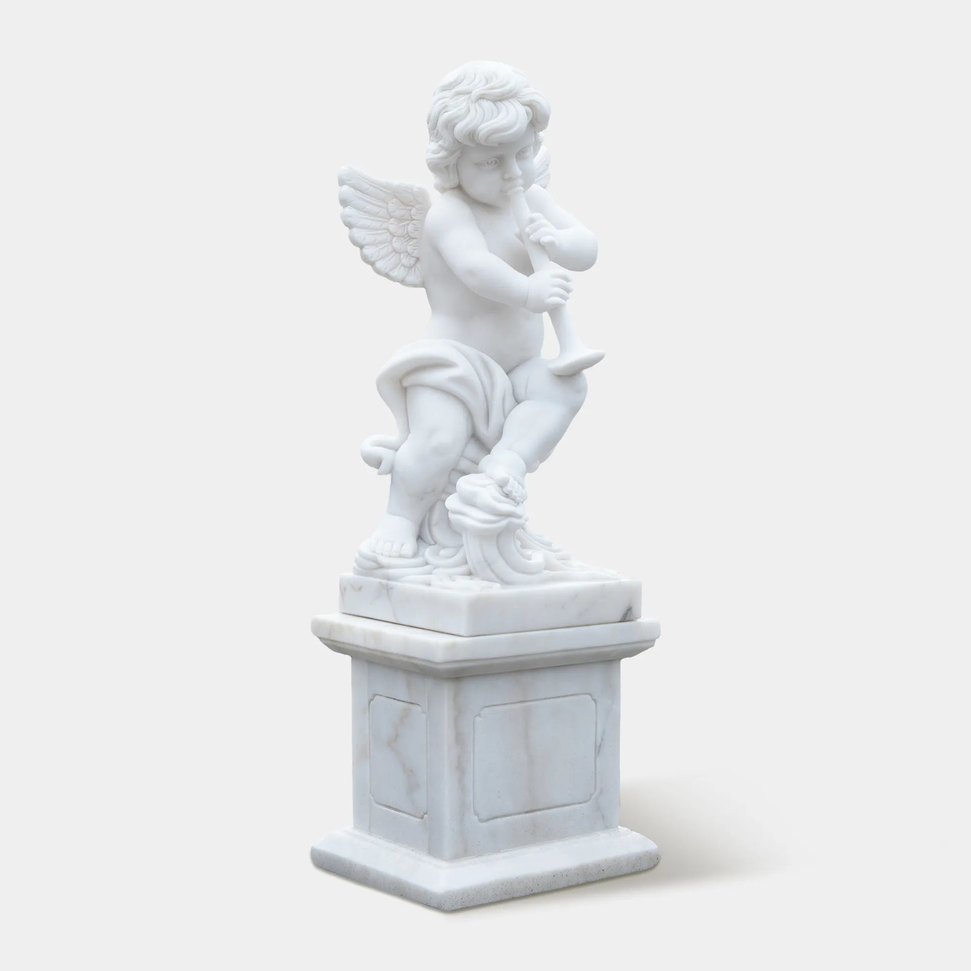 White marble cherub angel statue playing a flute on a pedestal in the garden path. 
