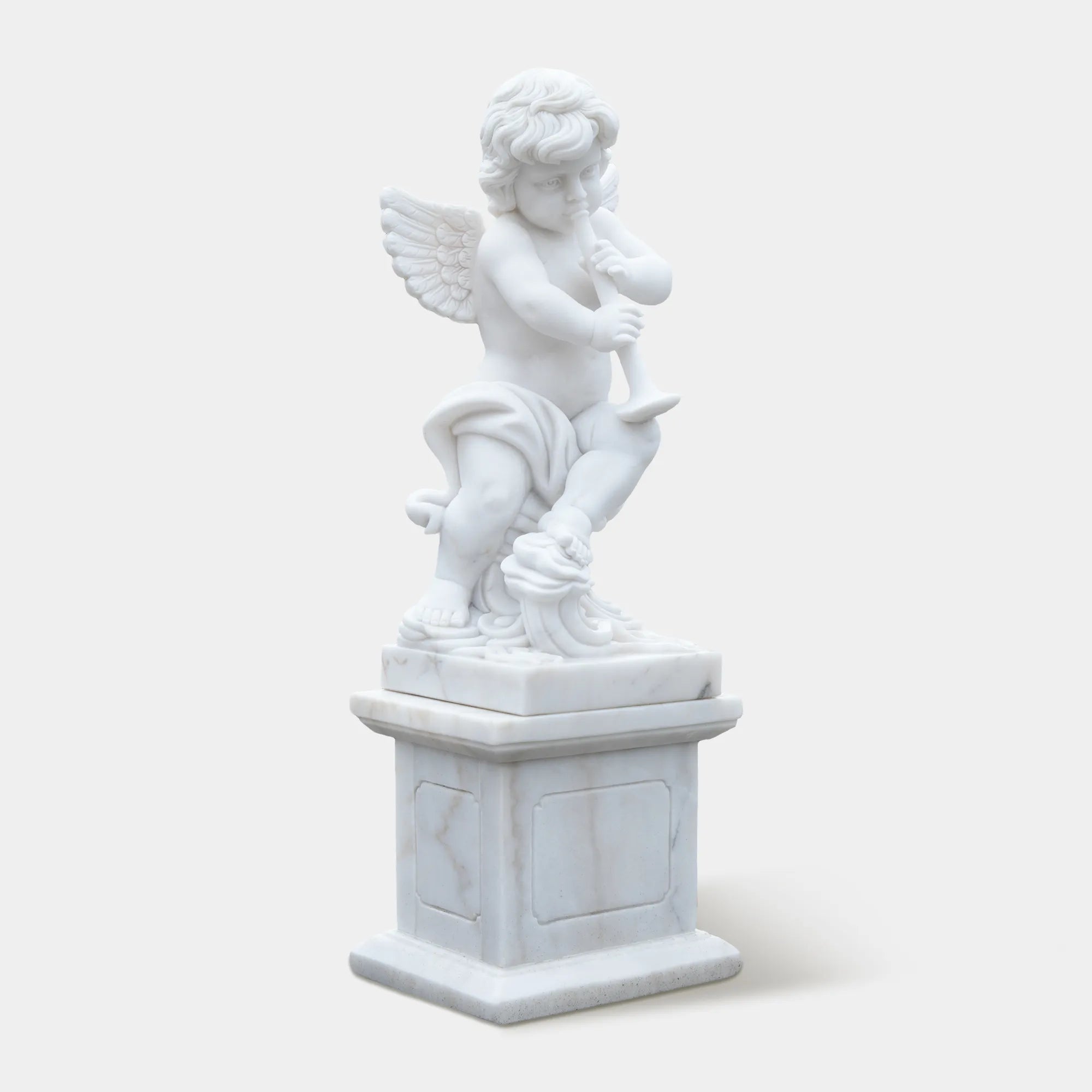 White marble cherub angel statue playing a flute on a pedestal in the garden path. 