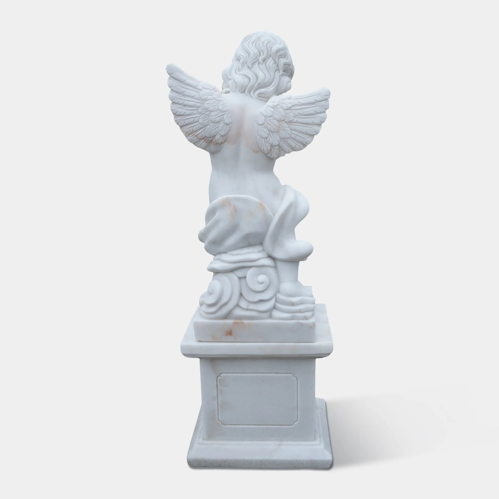 White marble cherub angel statue playing a flute on a pedestal in the garden path. 