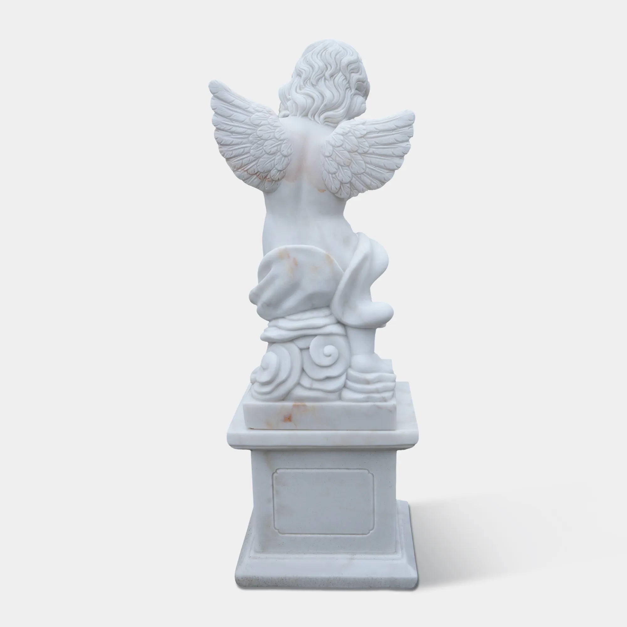 White marble cherub angel statue playing a flute on a pedestal in the garden path. 