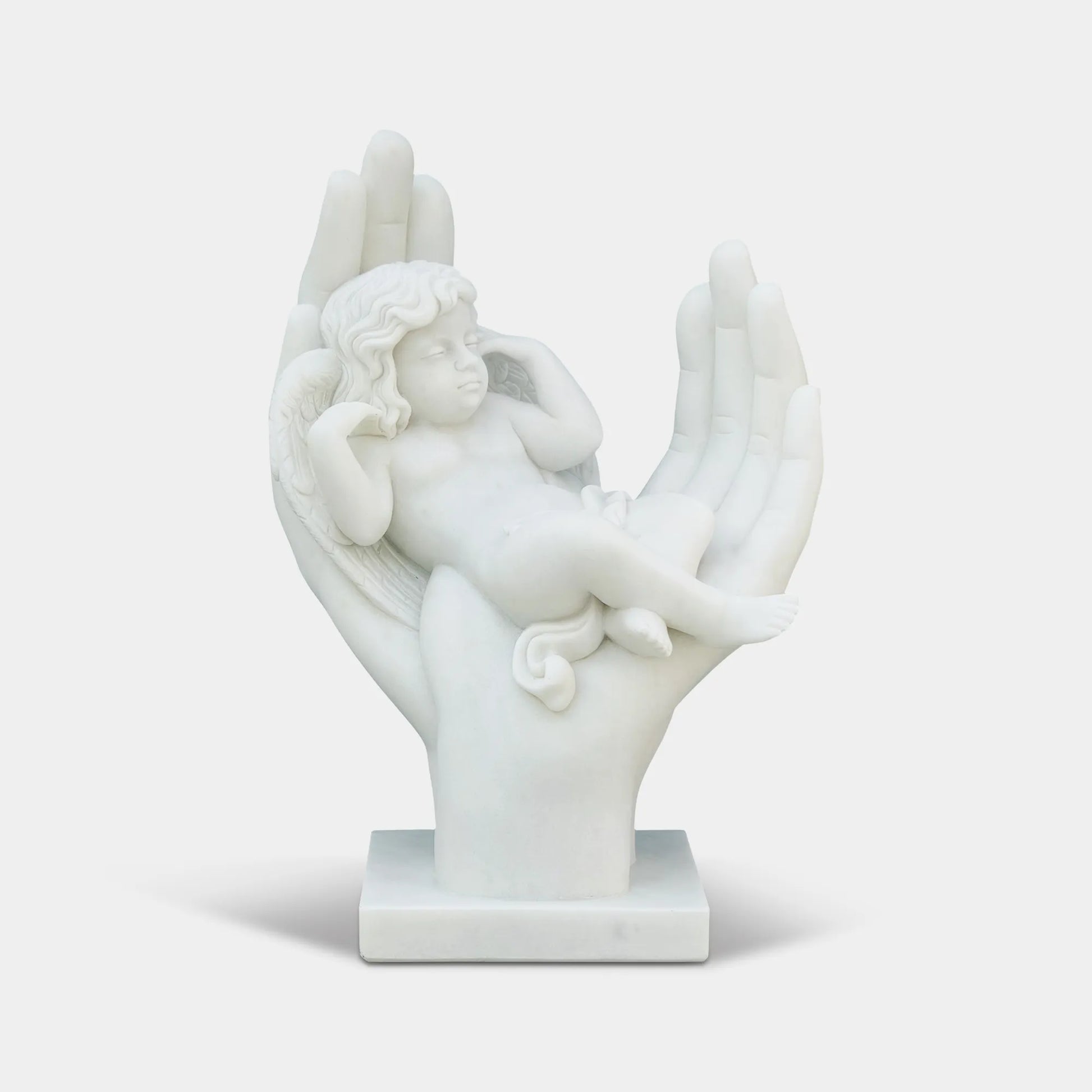 Marble cherub angel sculpture resting in large open hands in a formal garden courtyard in front of a classical building.