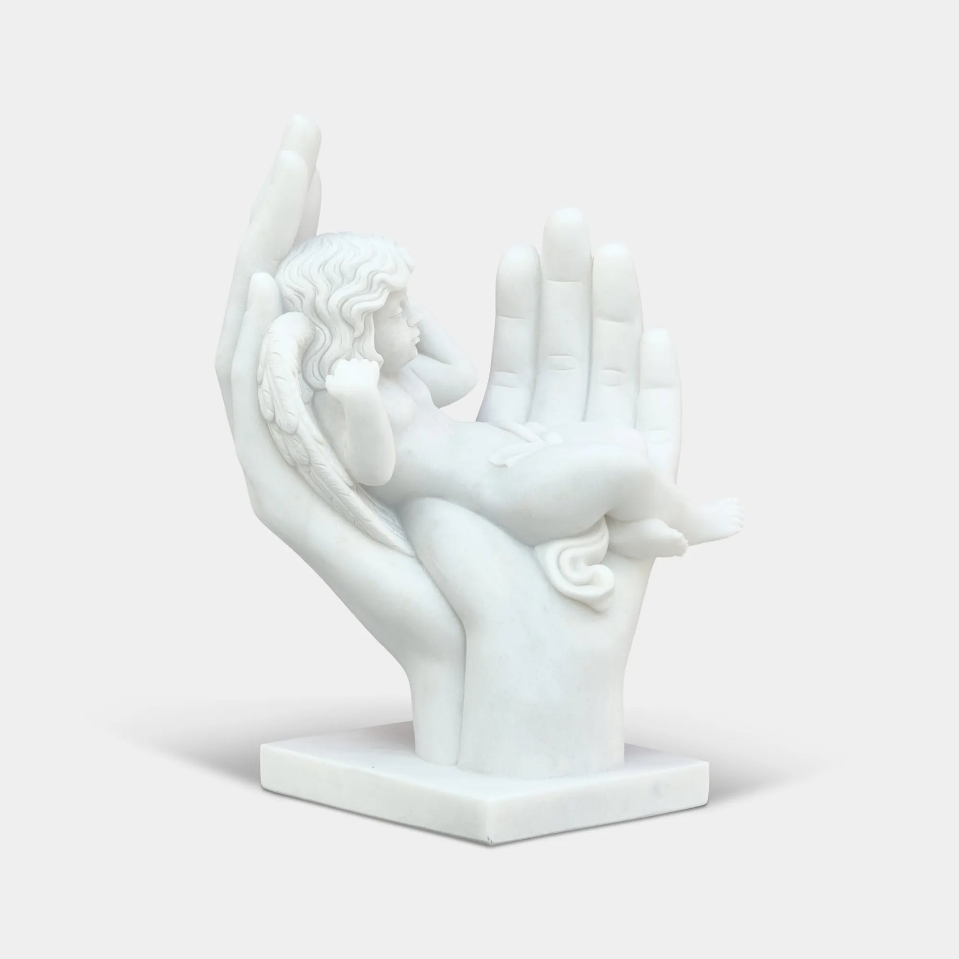 Marble cherub angel sculpture resting in large open hands in a formal garden courtyard in front of a classical building.