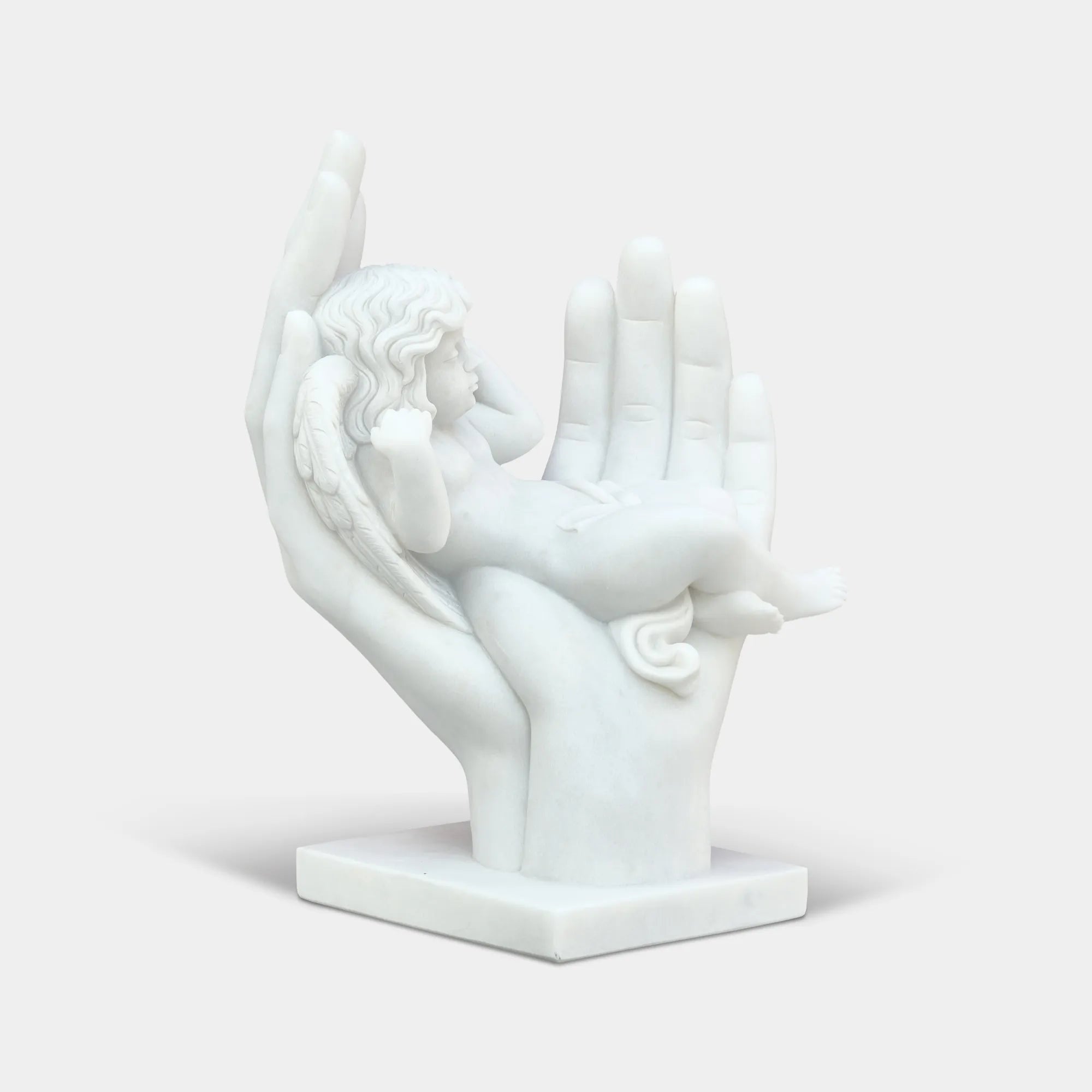 Marble cherub angel sculpture resting in large open hands in a formal garden courtyard in front of a classical building.