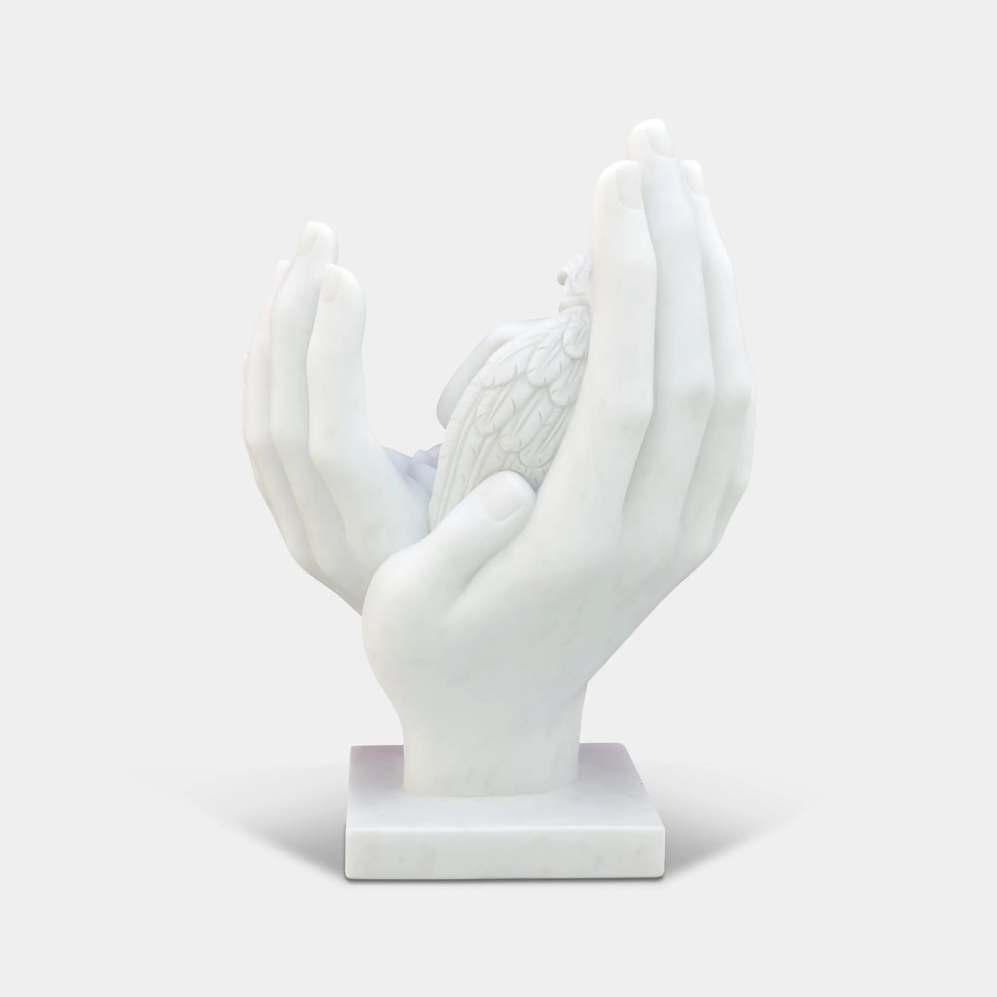 Marble cherub angel sculpture resting in large open hands in a formal garden courtyard in front of a classical building.