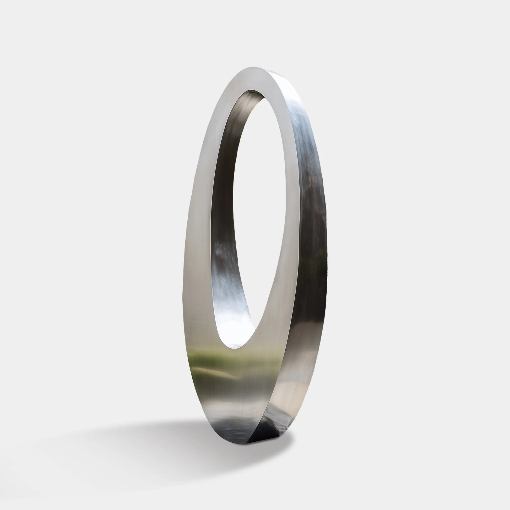 Polished stainless steel ring sculpture with an oval form placed in an outdoor landscape