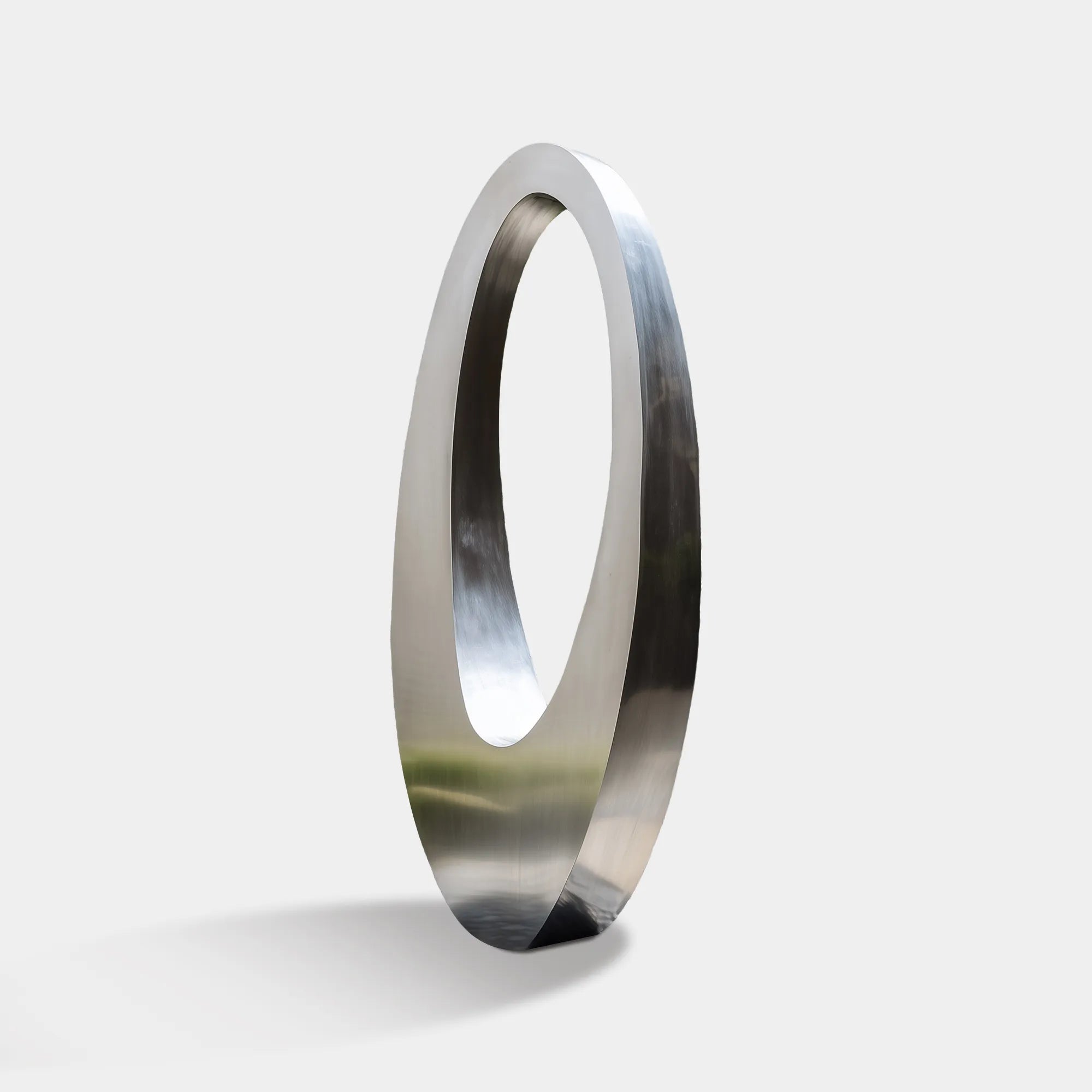 Polished stainless steel ring sculpture with an oval form placed in an outdoor landscape
