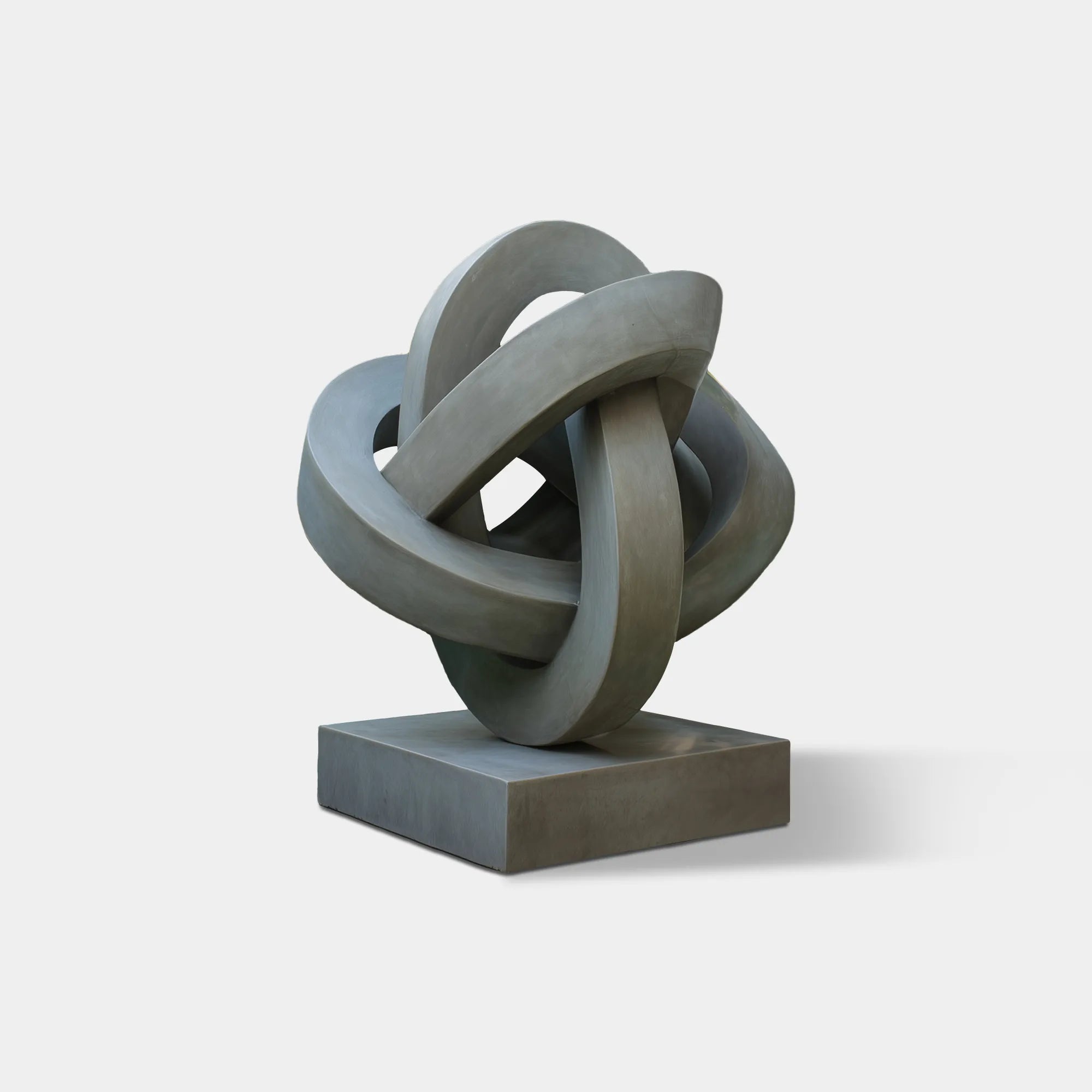 Abstract interwoven stainless steel ring sculpture displayed on a square base in a garden.