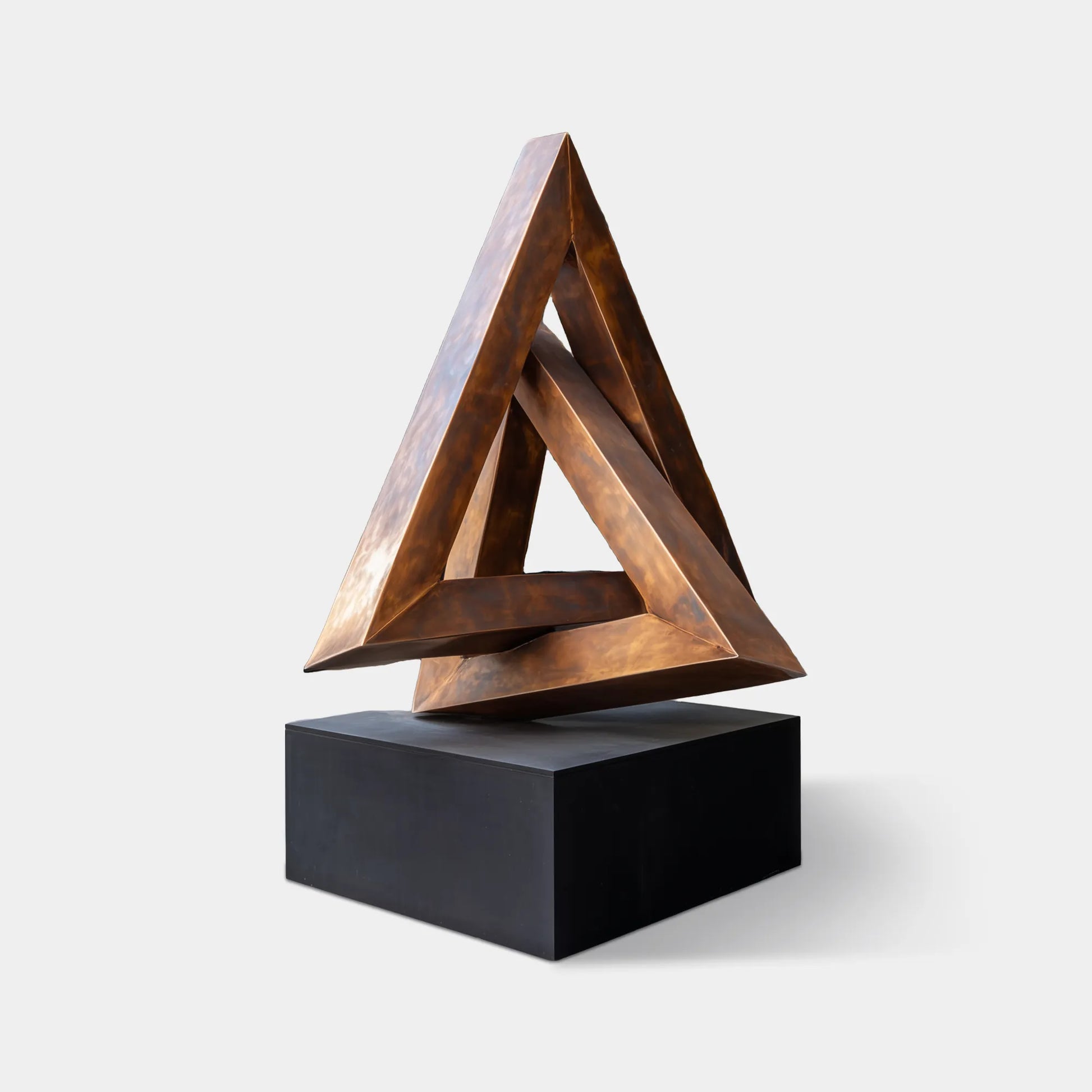 Bronze geometric triangle sculpture with layered form placed at a modern building entrance.