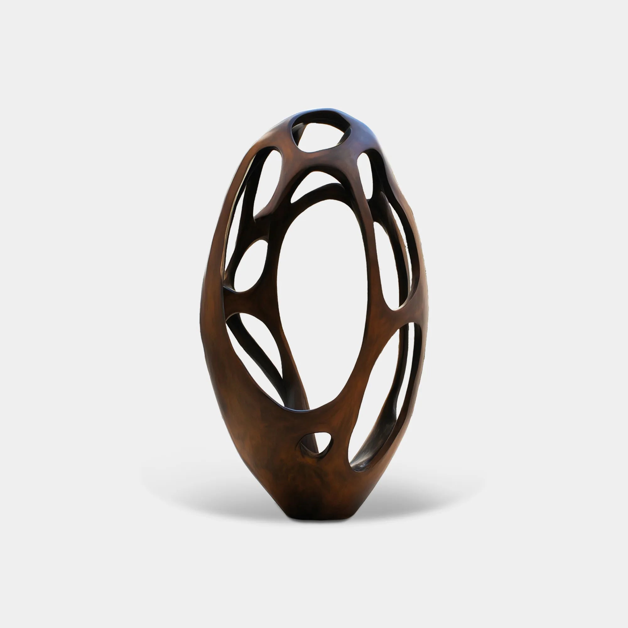 Hollow bronze abstract sculpture with open cut-out design in a modern courtyard with white walls and trees