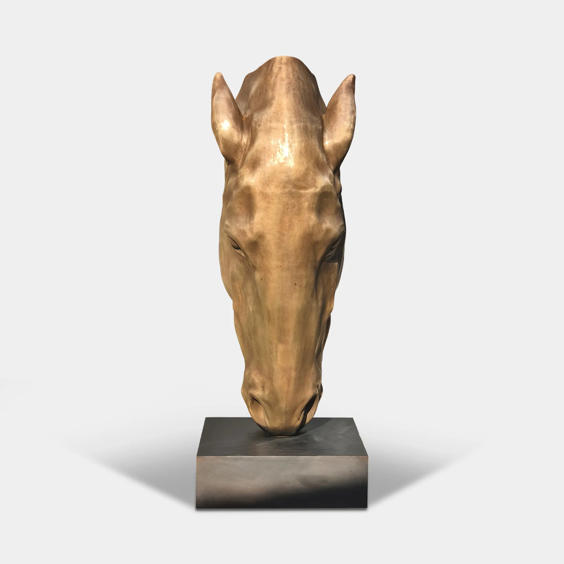 A bronze sculpture of a horse head in a garden with trees and a stone path.