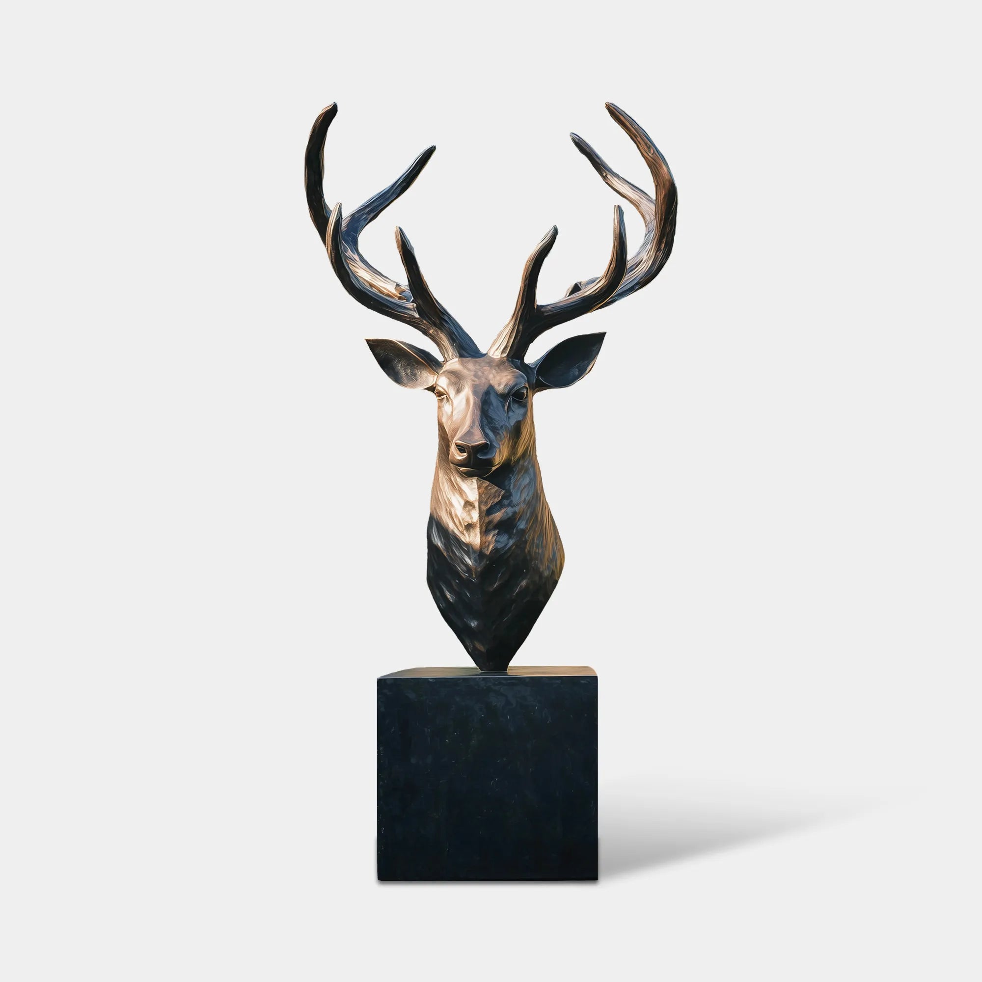 Bronze deer head bust sculpture with large antlers on pedestal in garden near stone wall.