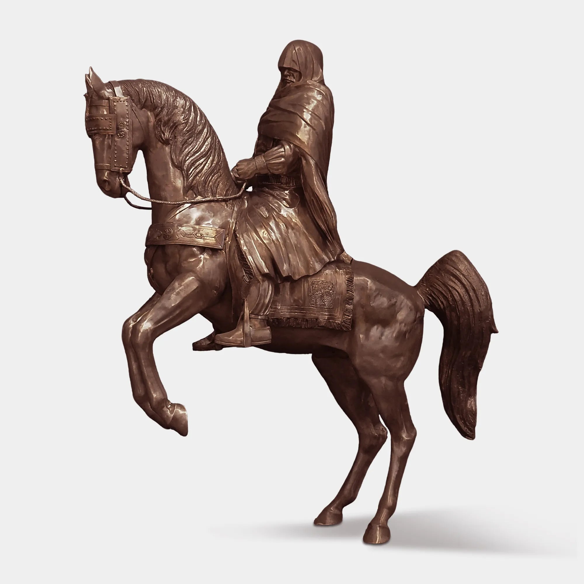 Bronze sculpture of a cloaked rider on a horse in dynamic motion in a villa garden.