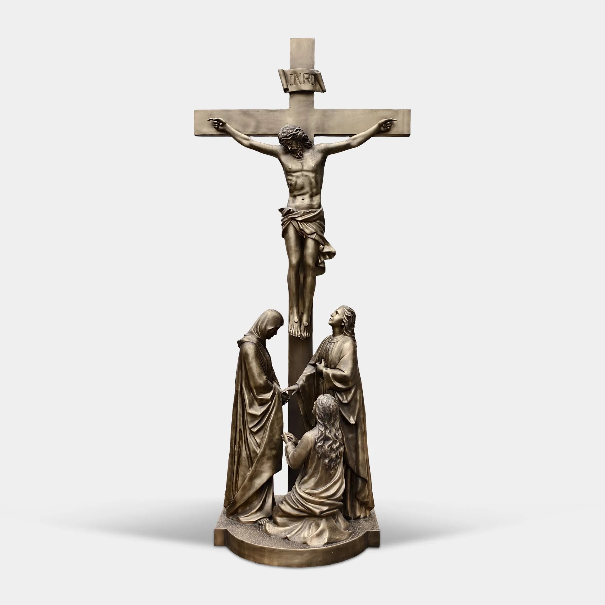 Bronze crucifix religious statue with Jesus on cross and St.Mary below in a garden near church.