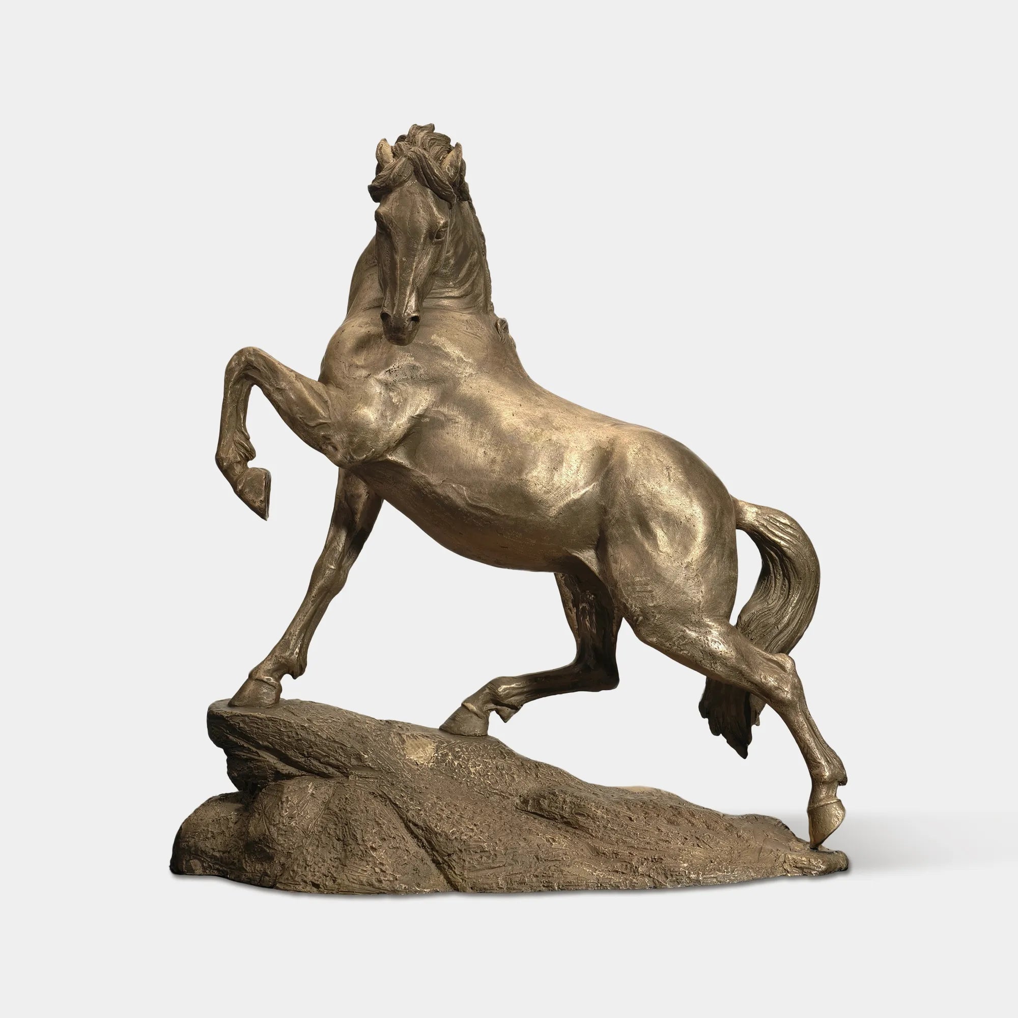 Bronze rearing horse statue on a rock base in grassy field with trees.