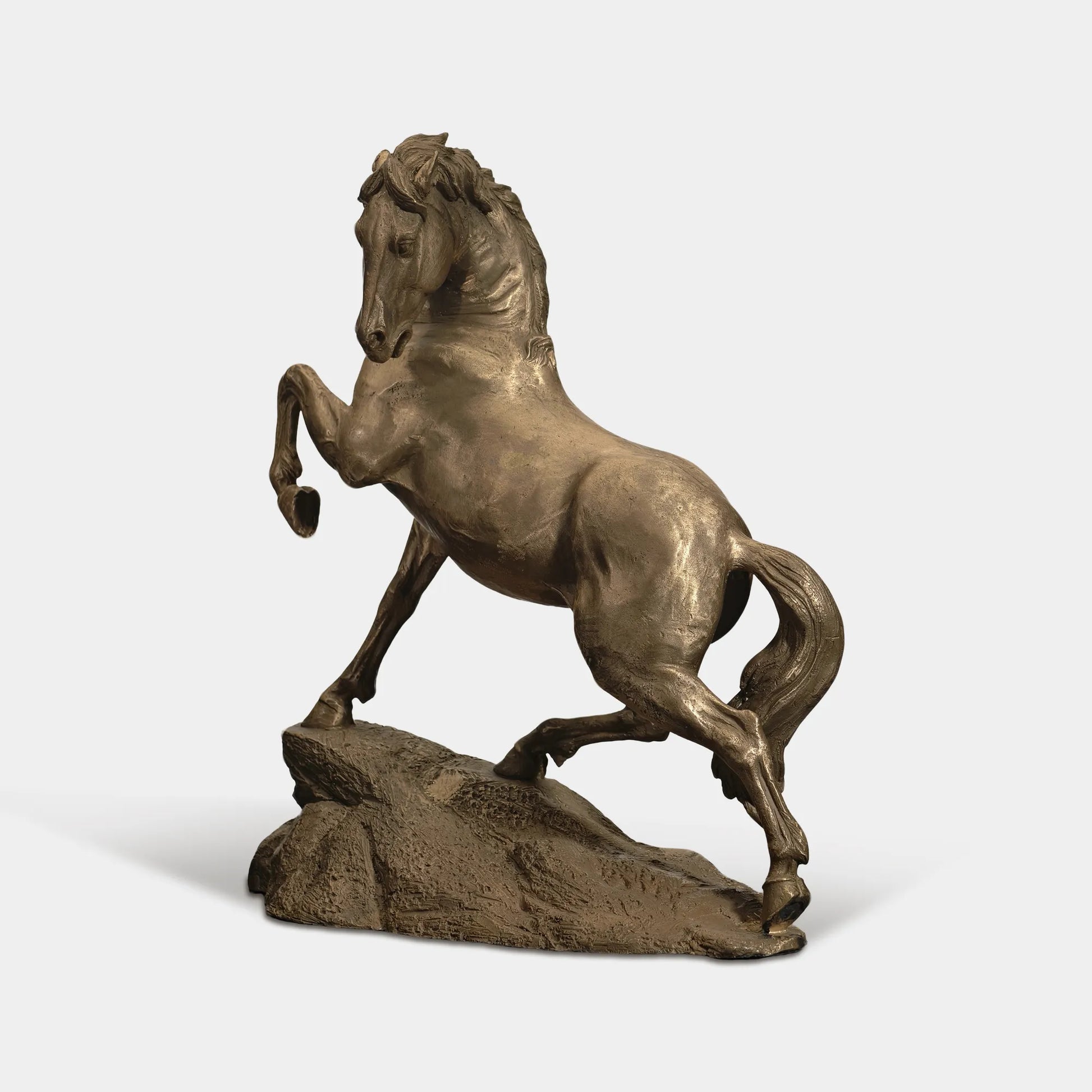 Bronze rearing horse statue on a rock base in grassy field with trees.