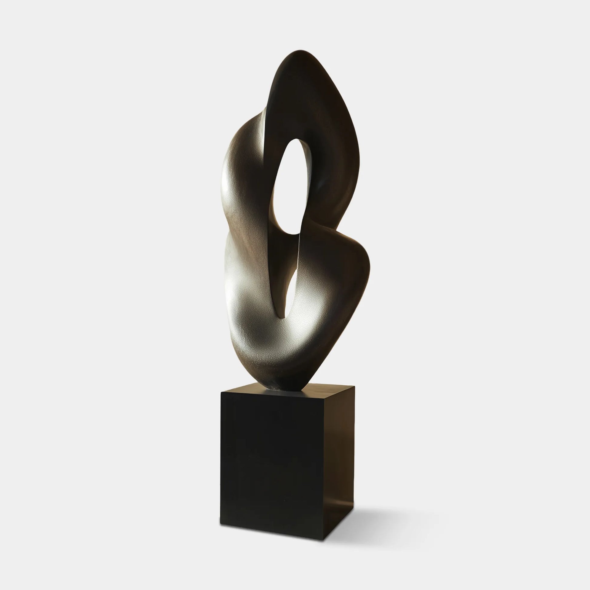 Abstract bronze sculpture in hollow organic form with base near window in modern living room.