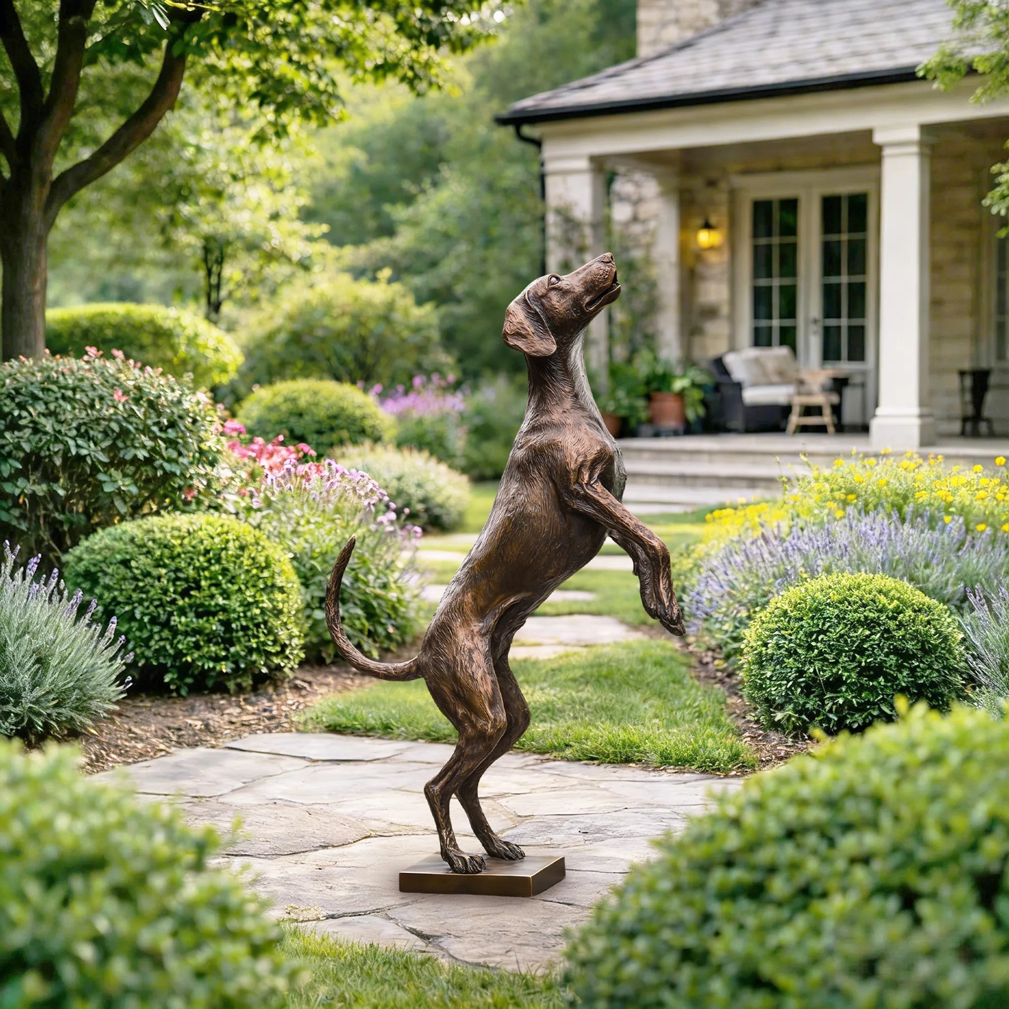 Bronze dog sculpture standing on hind legs in a garden with trimmed shrubs and flowers. 