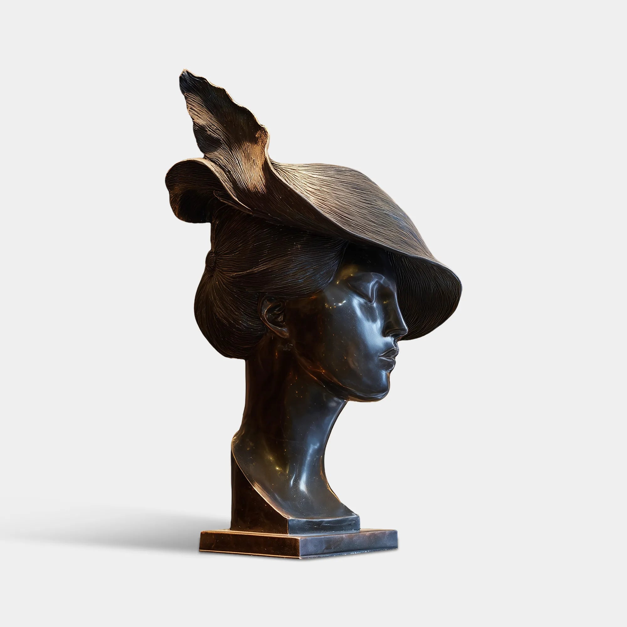Bronze bust sculpture of a woman wearing a wide flowing hat on a table.