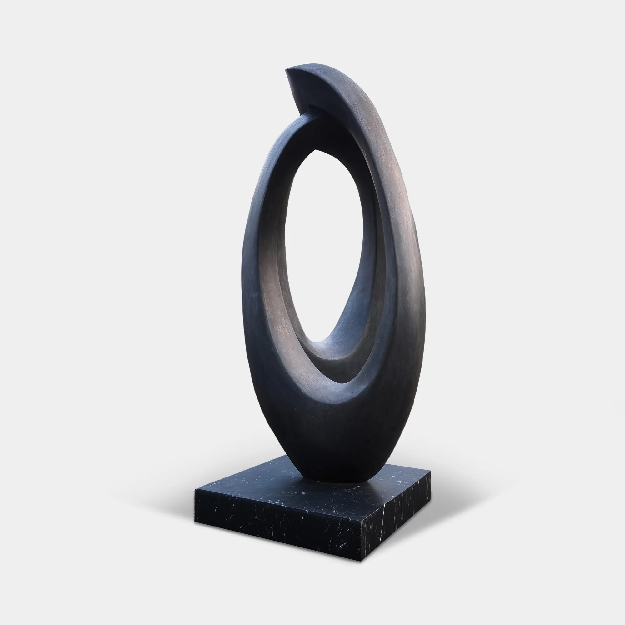 Dark bronze organic form sculpture on a black stone base in a modern zen courtyard garden.