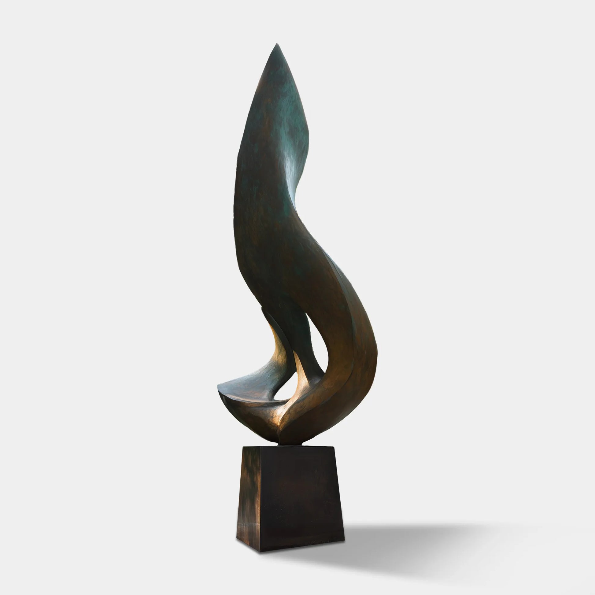 Patinated bronze flowing form sculpture on a pedestal in front of a modern residence with surrounding trees and landscaped garden.