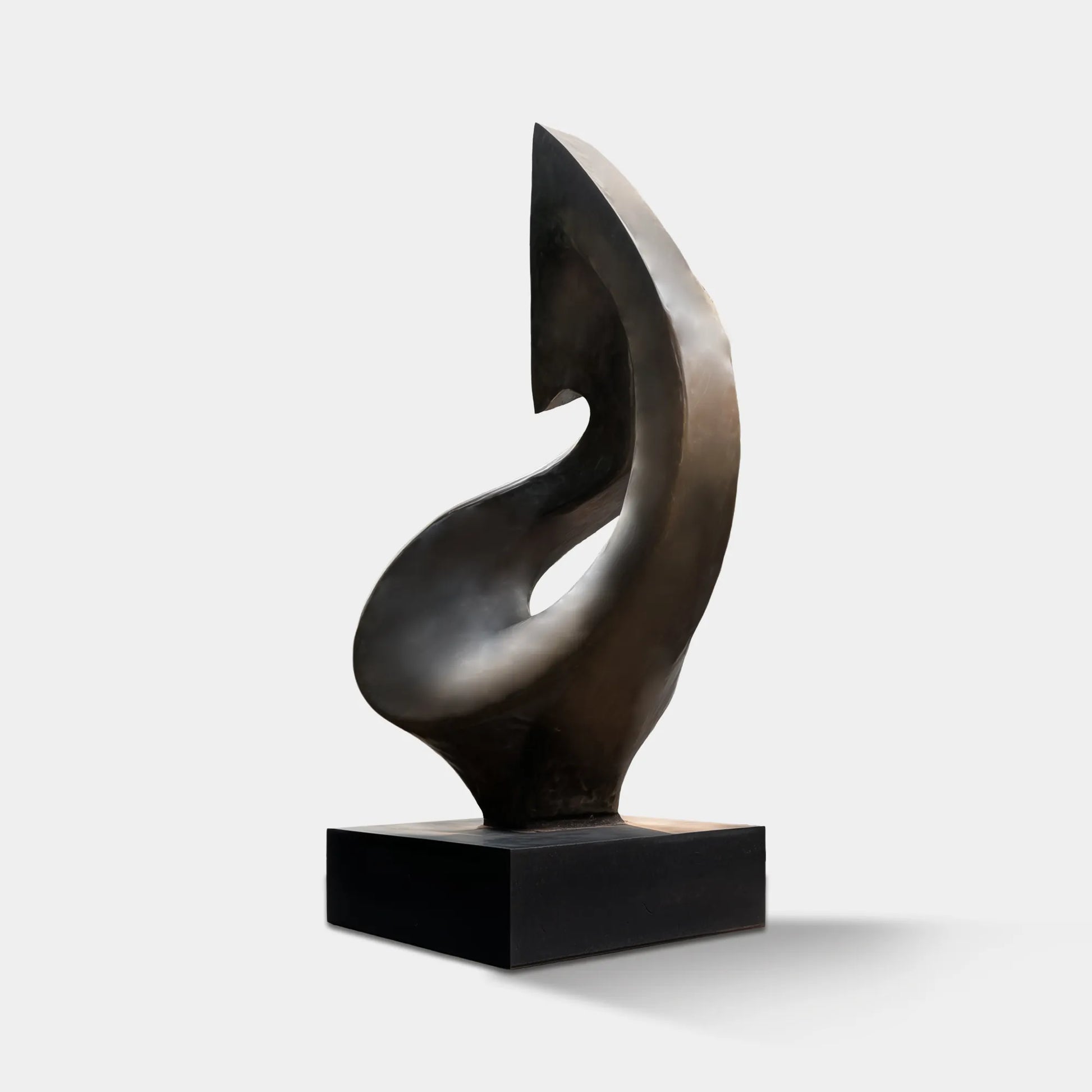 Dark bronze organic form sculpture on a rectangular pedestal in front of a modern residence with surrounding trees and landscaped greenery.
