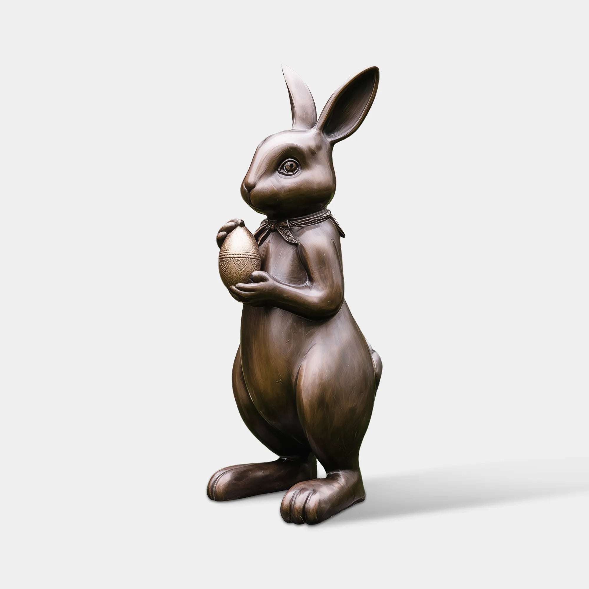 Bronze rabbit statue holding an Easter egg in a front garden near a residential entryway.