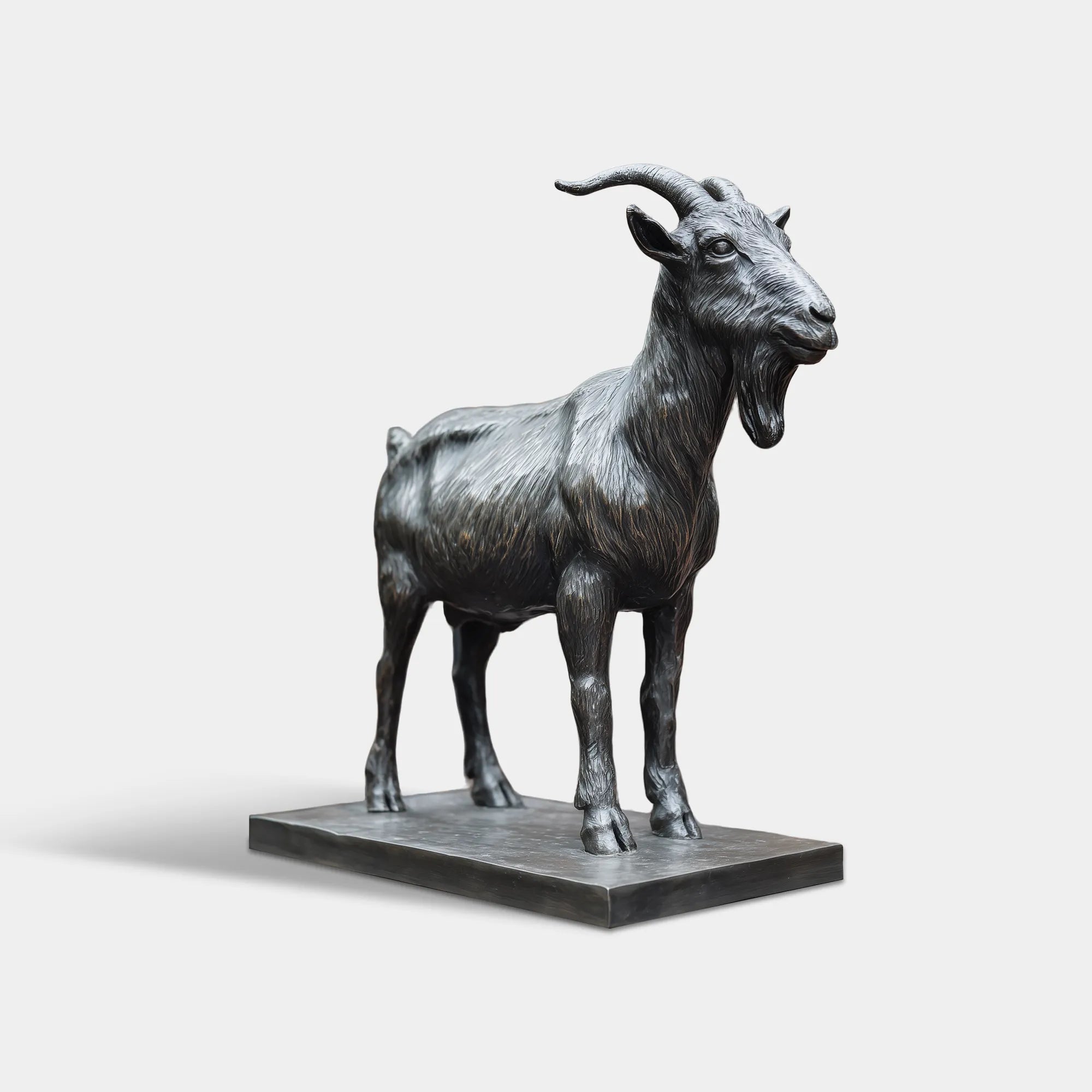 A realistic bronze goat sculpture stands outdoors, with a black iron fence and red brick wall in the background.