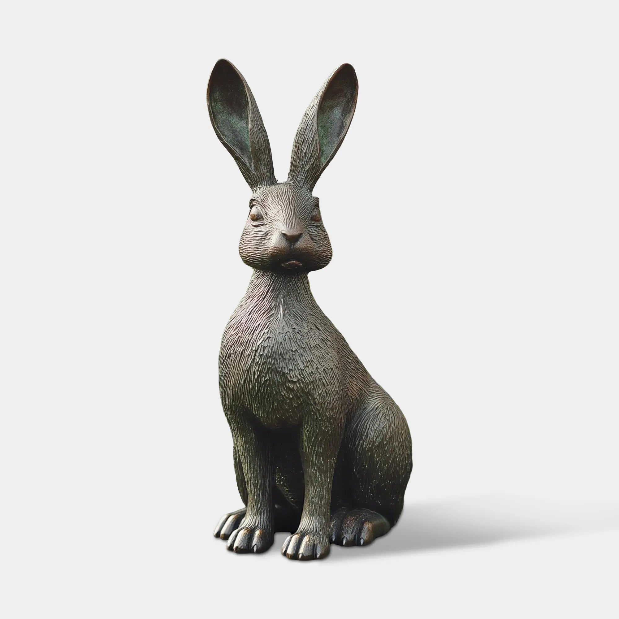 A bronze sitting hare sculpture stands on green grass amid blooming flowers beside a white house.