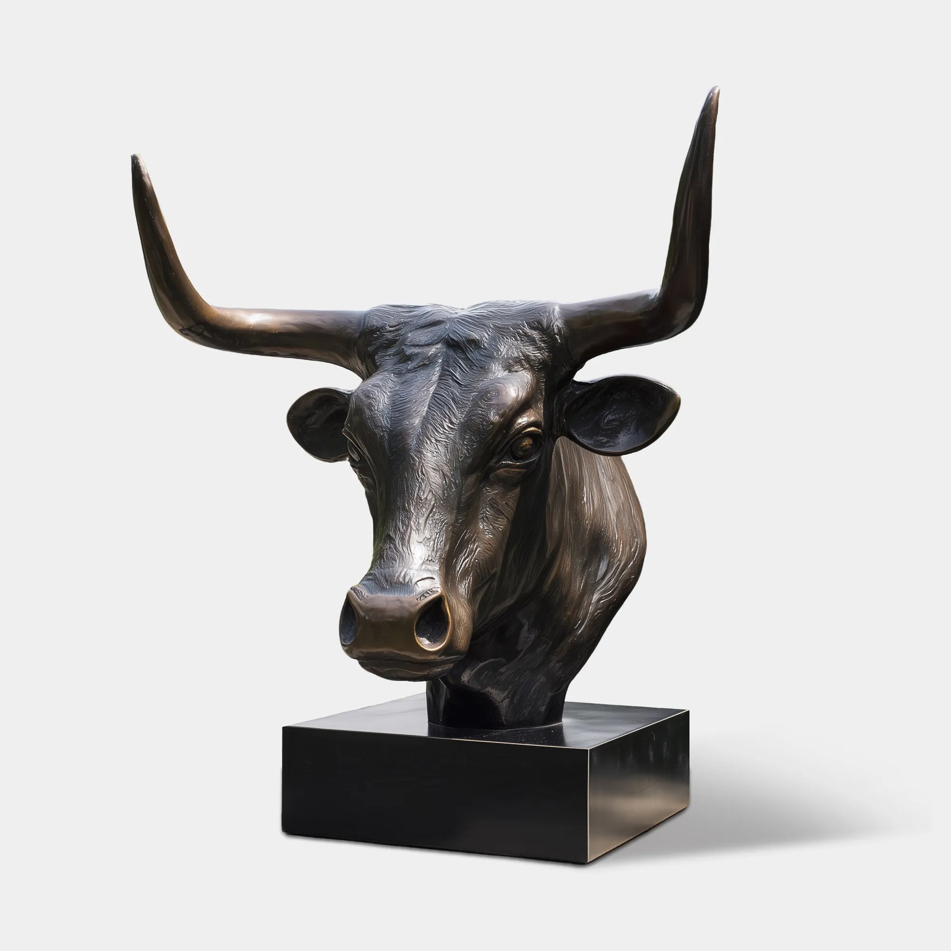 Bronze bull head sculpture with detailed horns and textured surface on base in ranch entrance. 