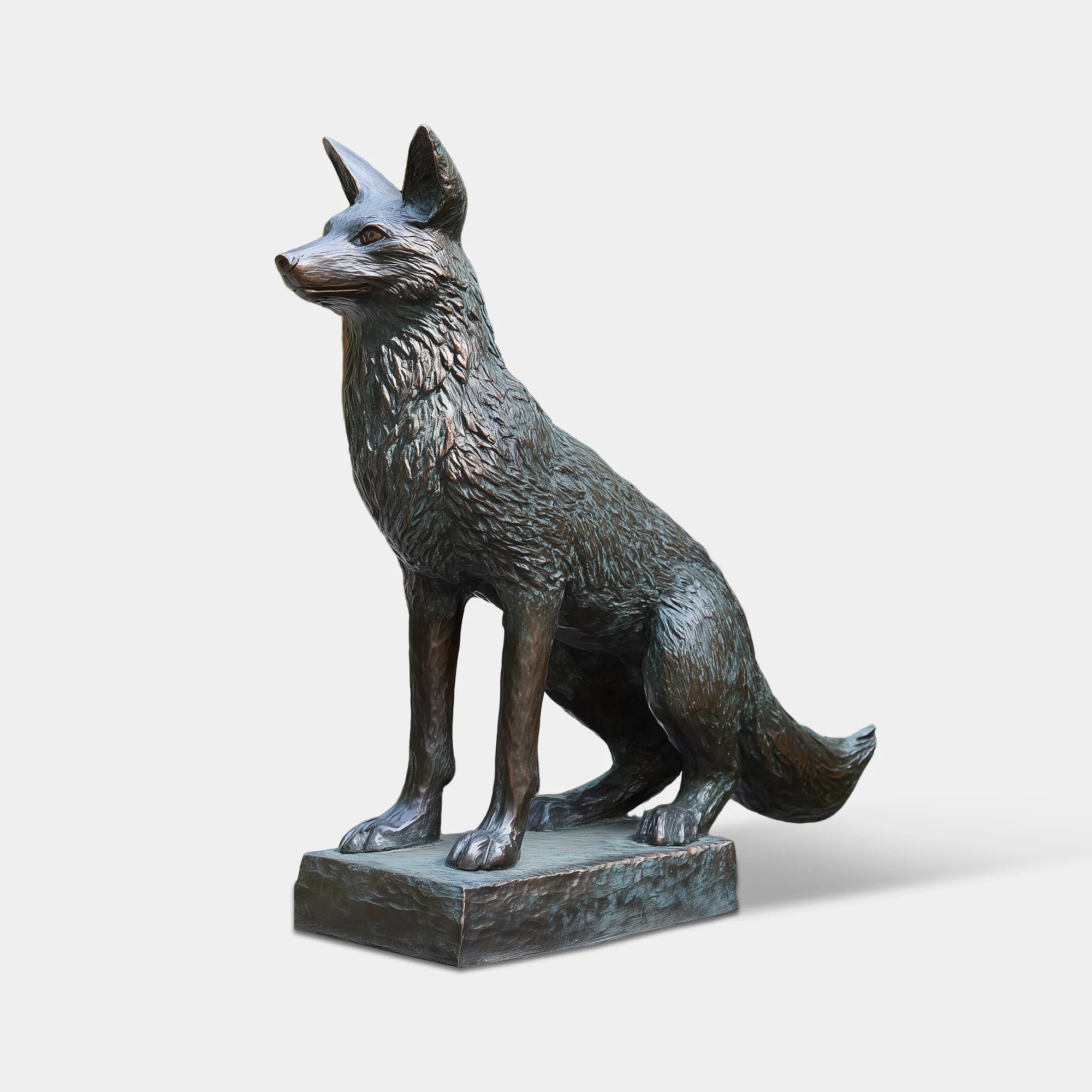 This patina bronze fox sculpture stands on stone porch steps before wooden railings and green leafy trees.