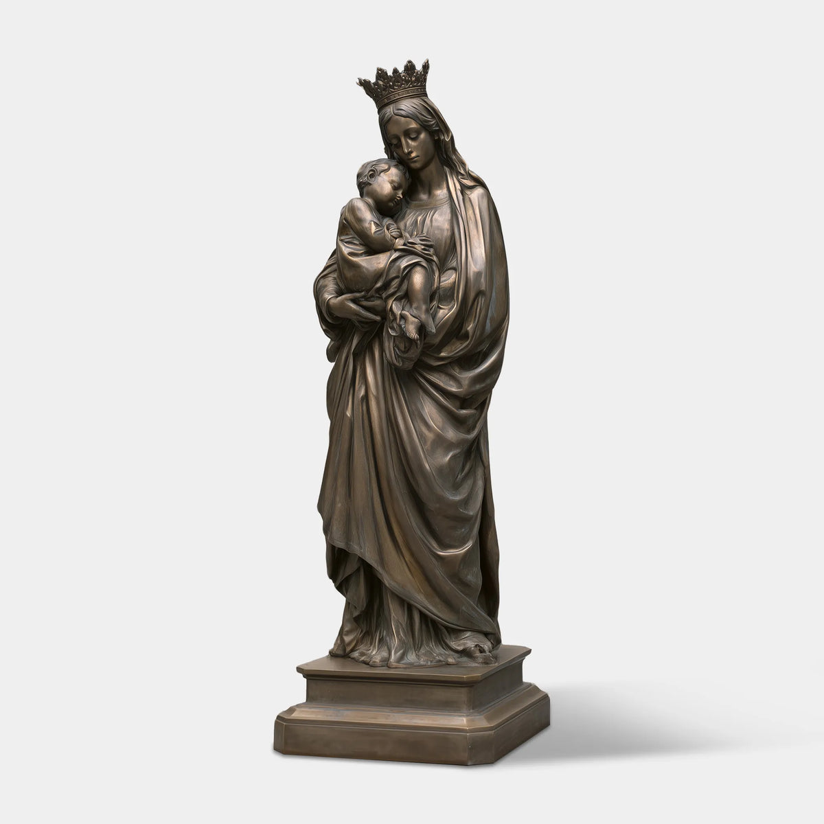 A bronze Virgin Mary and Baby Jesus Statue stands beside a light building.
