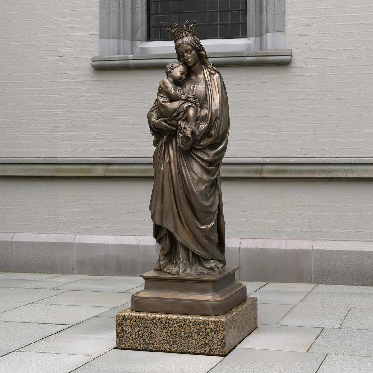 A bronze Virgin Mary and Baby Jesus Statue stands beside a light building.