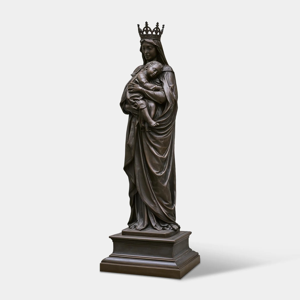 A bronze Virgin Mary with Baby Jesus statue stands in an open plaza with classic church buildings.