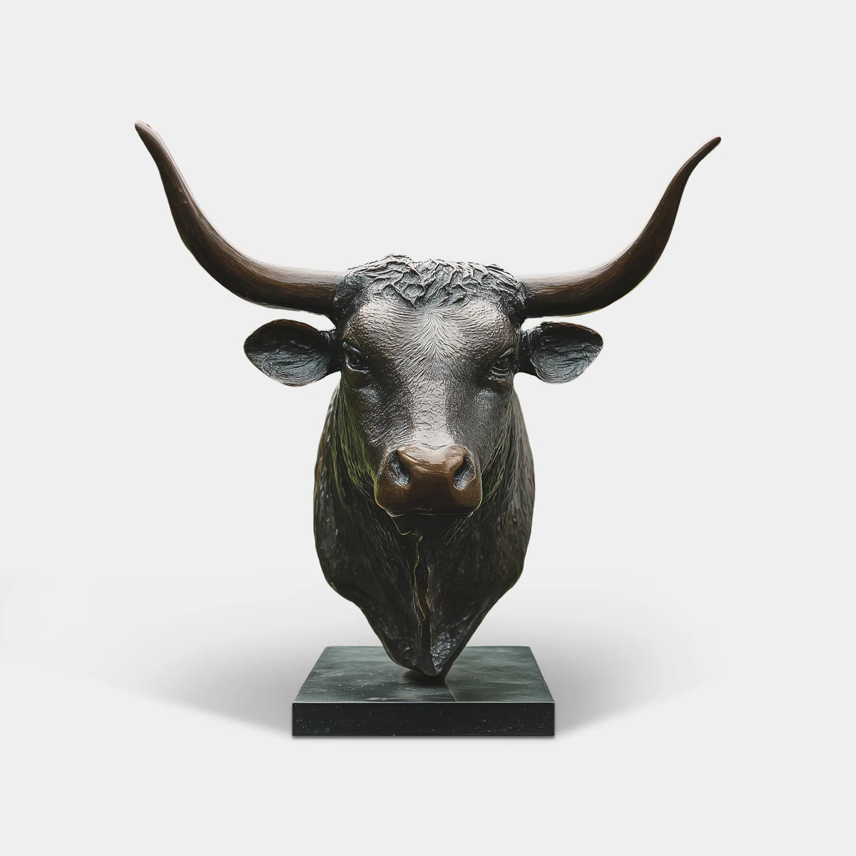 Dark bronze longhorn bull head statue with wide curved horns on a black pedestal in a country estate garden.