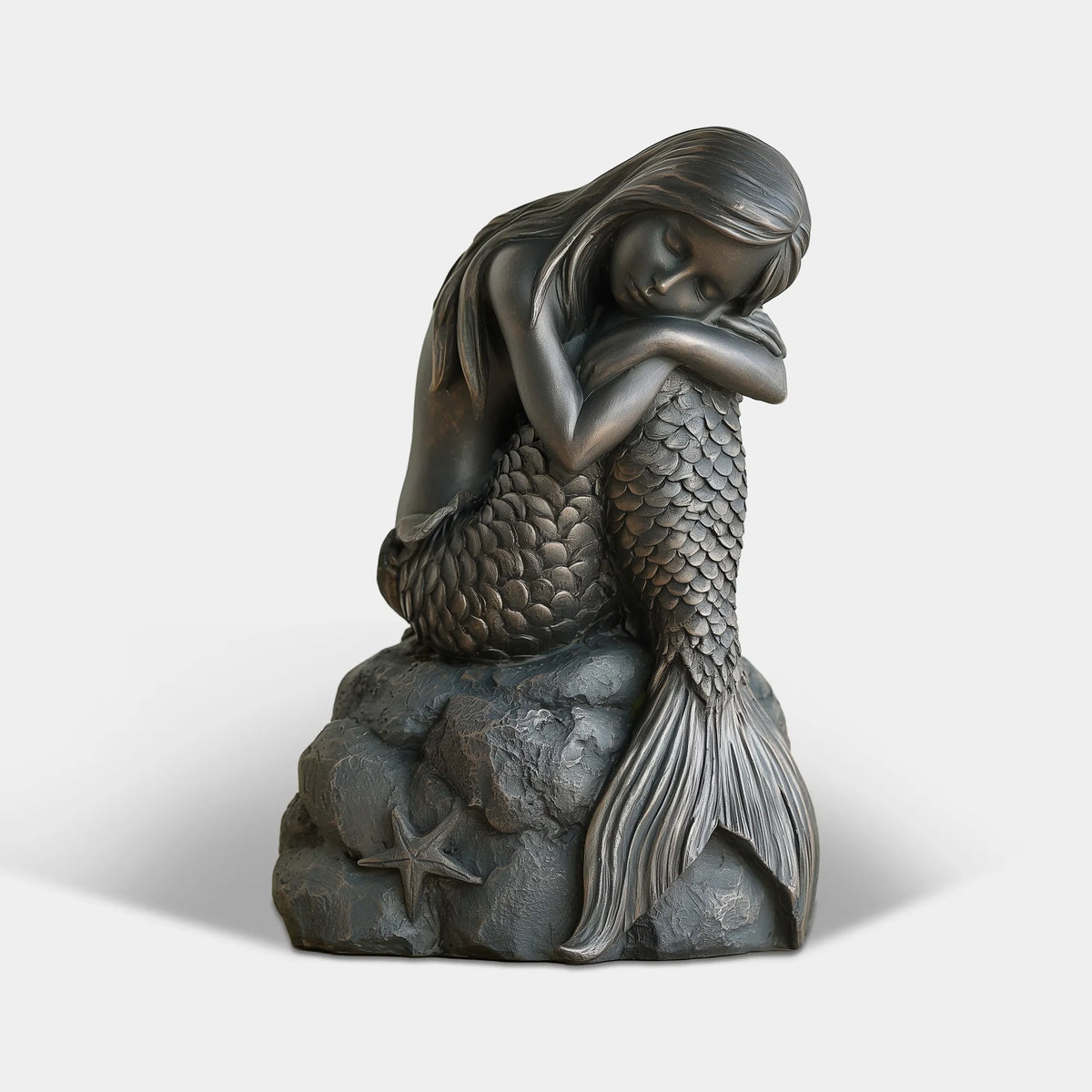 A bronze sleeping mermaid statue rests on a rock base with starfish decoration.