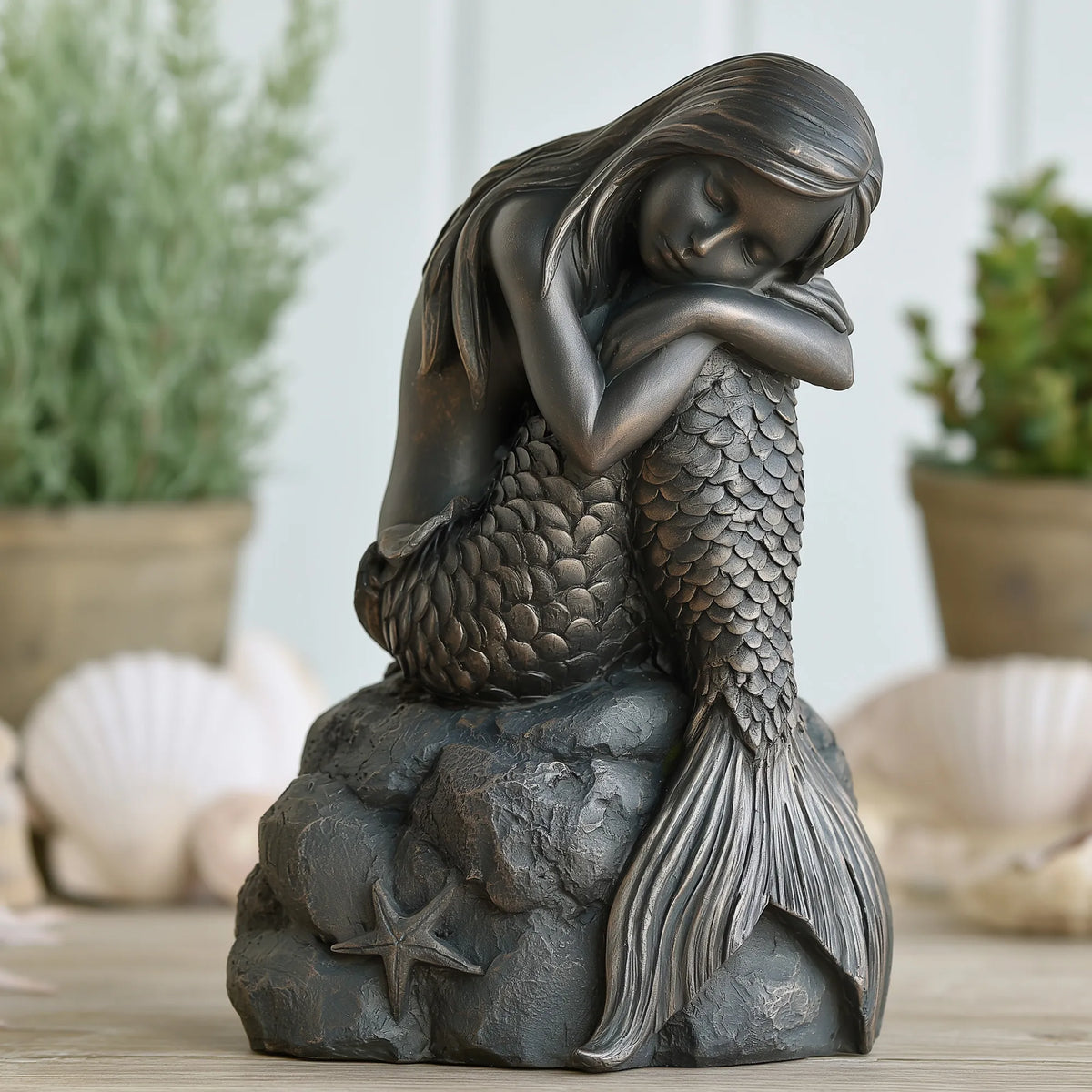A bronze sleeping mermaid statue rests on a rock base with starfish decoration.