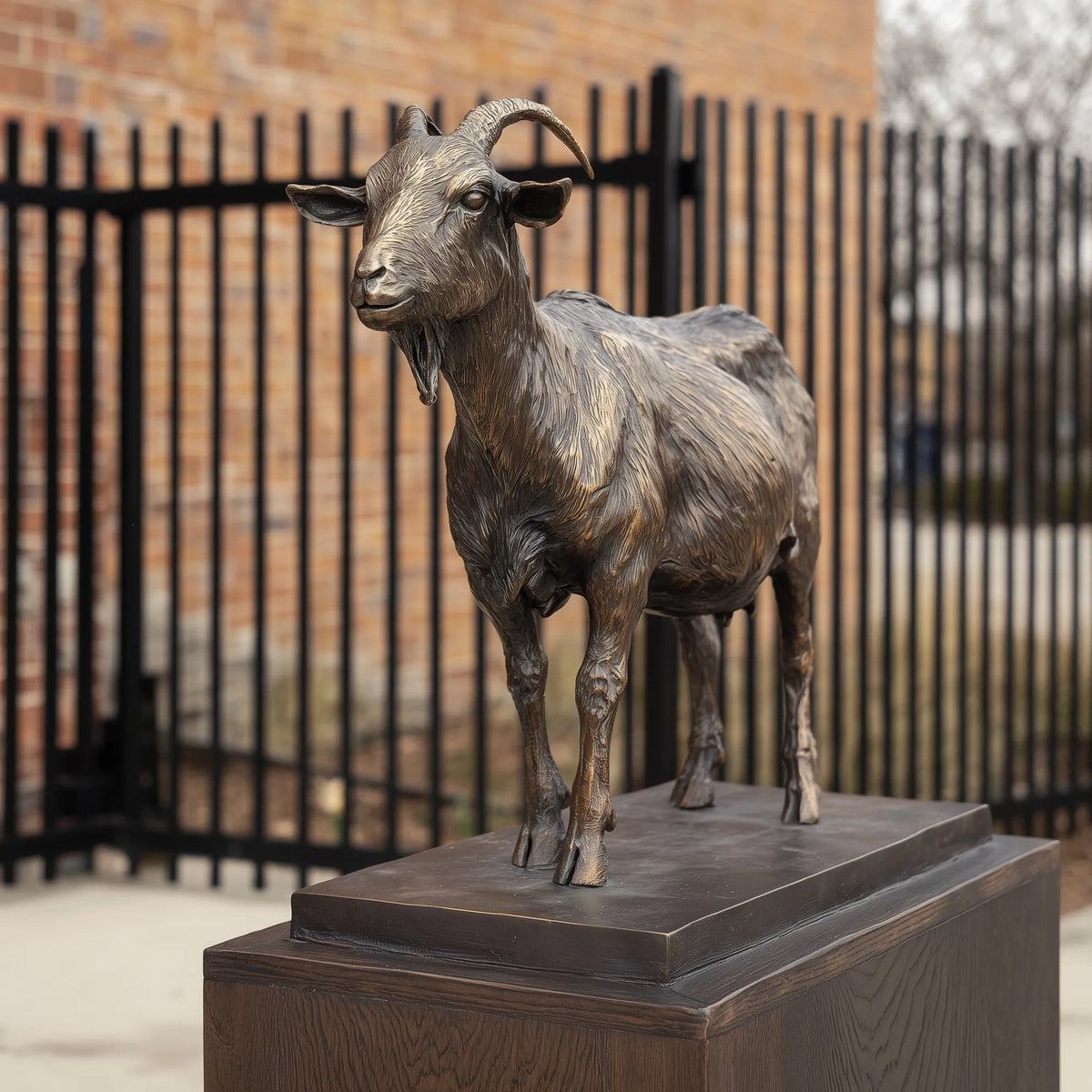 Bronze standing goat statue beside an outdoor entrance gate.