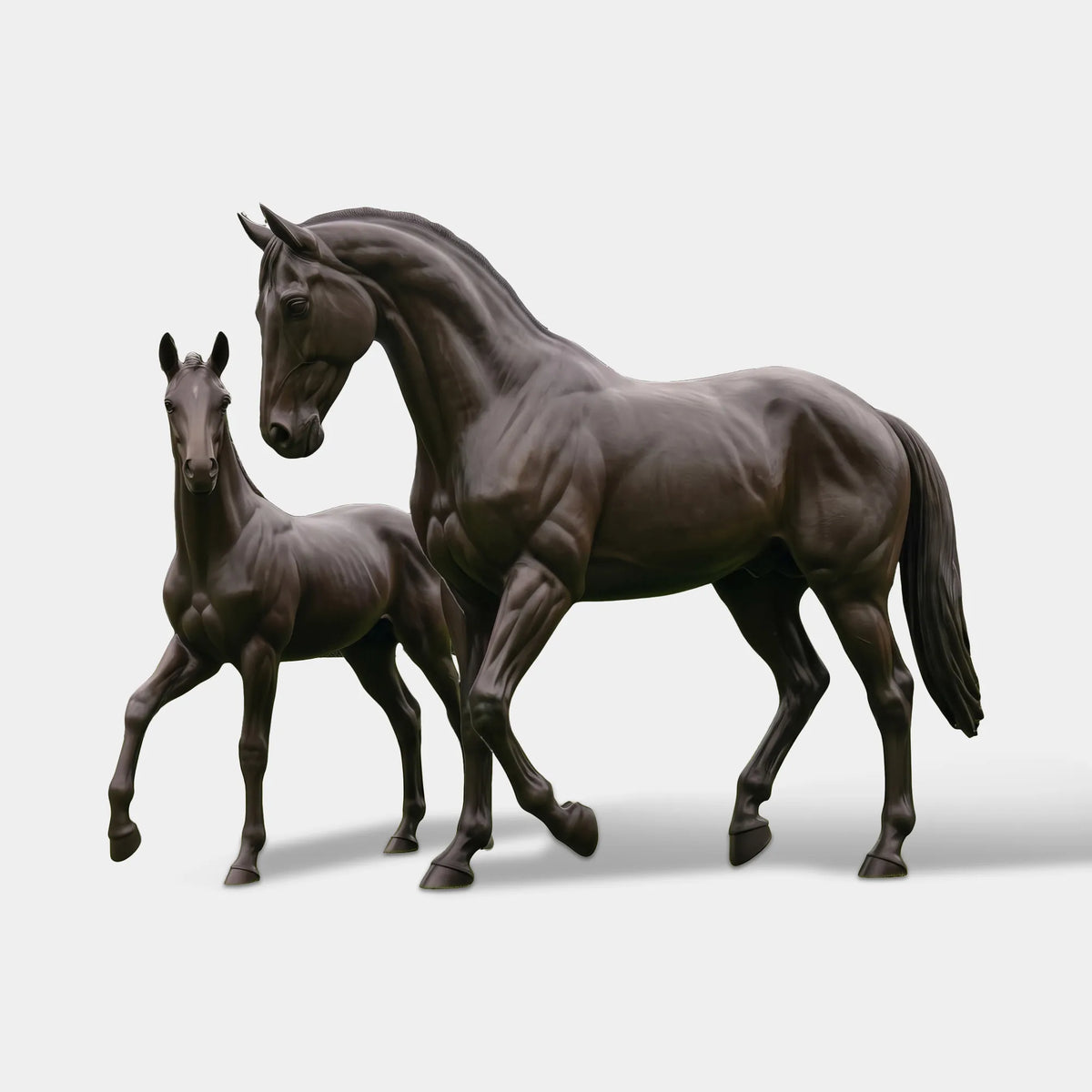 Dark bronze mare and foal sculpture with realistic muscular details, gently lowered heads, and walking poses on a lawn surrounded by manicured hedges and tall trees.