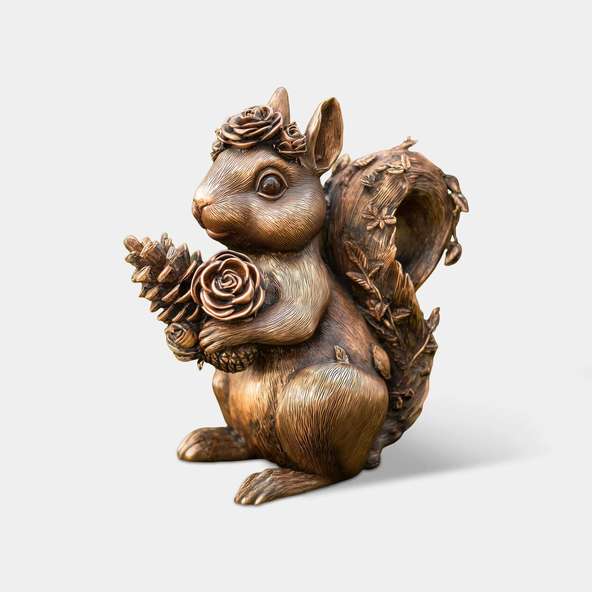 Antique bronze squirrel statue holding roses and pinecones with floral decorations on its curled tail on a moss-covered tree stump. 