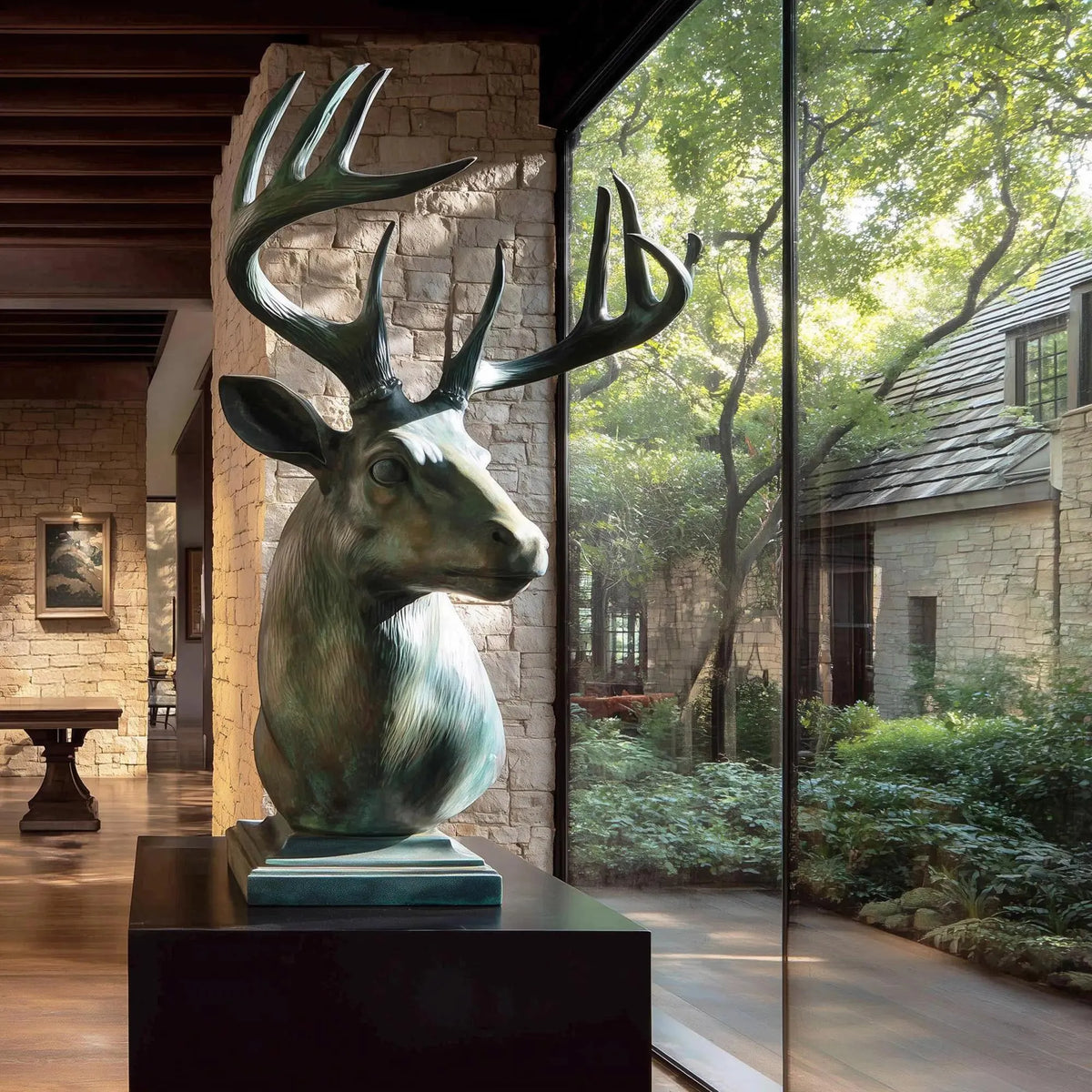 Large bronze deer bust sculpture with branching antlers, realistic facial details and green patina finish beside floor-to-ceiling windows.