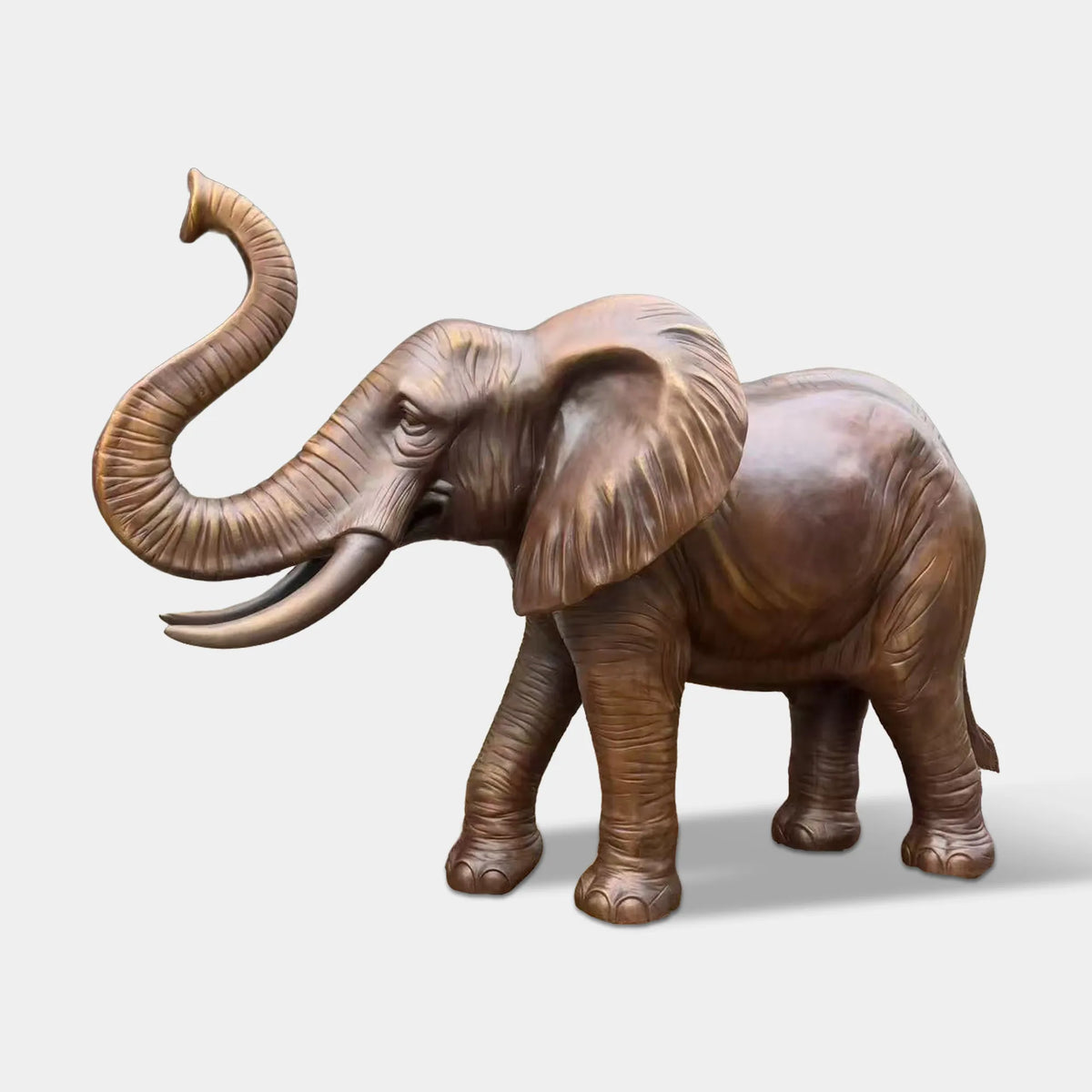 A bronze elephant statue with raised trunk stands along a shaded park walking path.