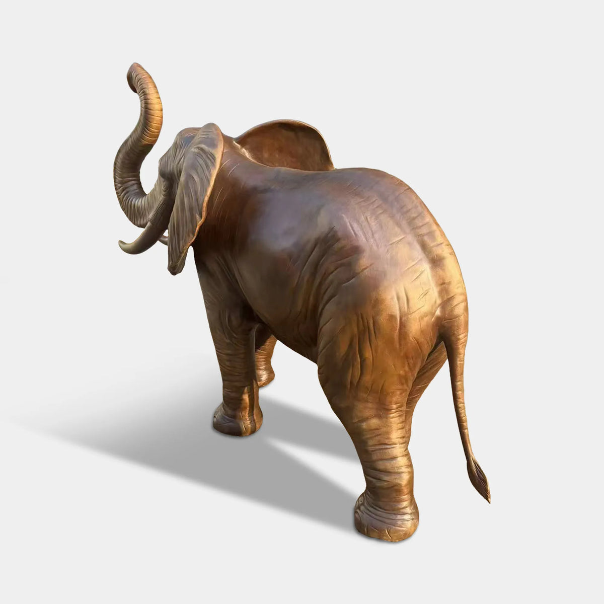A bronze elephant statue with raised trunk stands along a shaded park walking path.